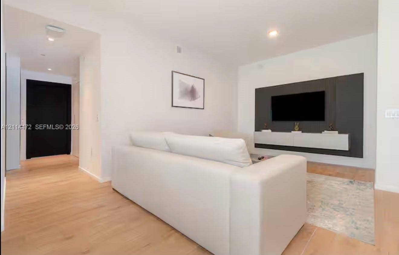 398 NE 5th Street, #4001, Miami, FL 33132 Living area featuring wood-finish flooring, a charcoal-toned paneled accent wall, a floating built-in console, and a solid black entry door