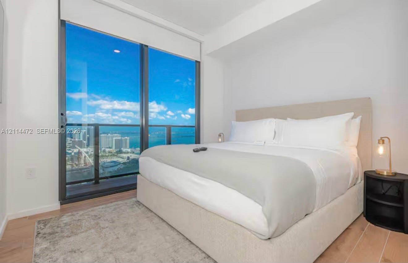 398 NE 5th Street, #4001, Miami, FL 33132 Floor-to-ceiling glass sliding doors, private balcony, wood-finish flooring, and expansive urban and water scenery