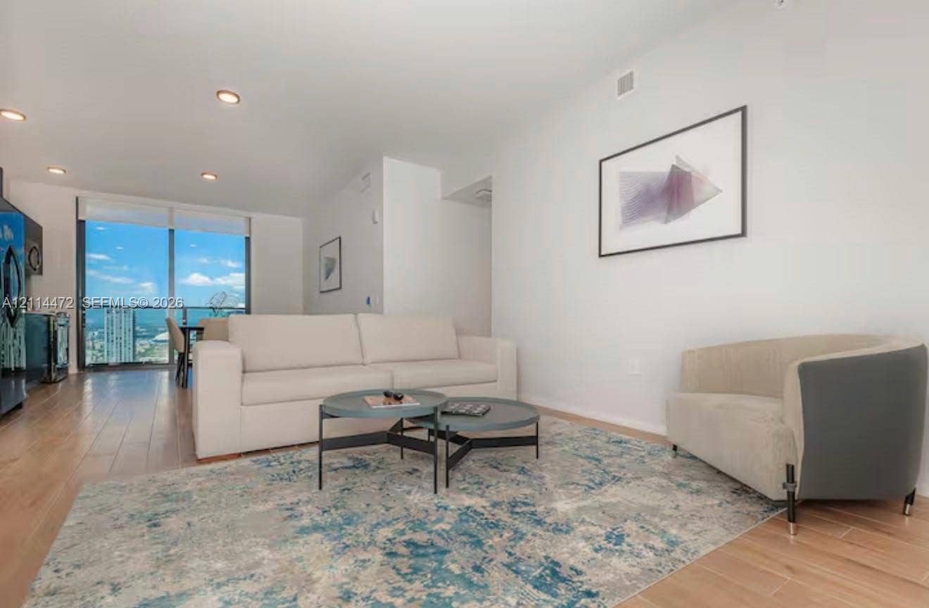 398 NE 5th Street, #4001, Miami, FL 33132 Open-concept living space featuring wood-finish flooring, recessed lighting, and floor-to-ceiling glass paneling with balcony access