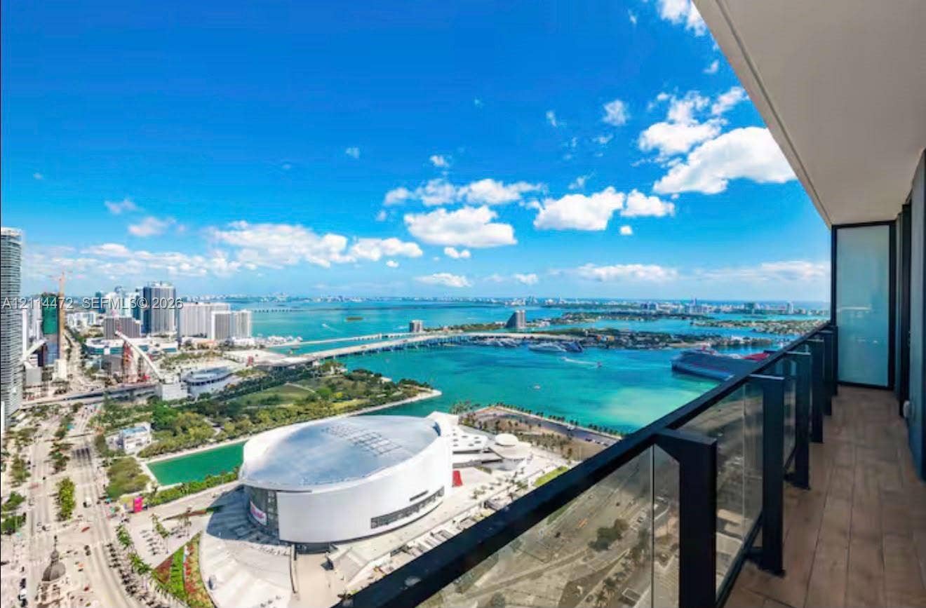 398 NE 5th Street, #4001, Miami, FL 33132 Covered balcony featuring wood-finish flooring and a glass railing with black metal framing, showcasing an expansive waterfront and city skyline panorama