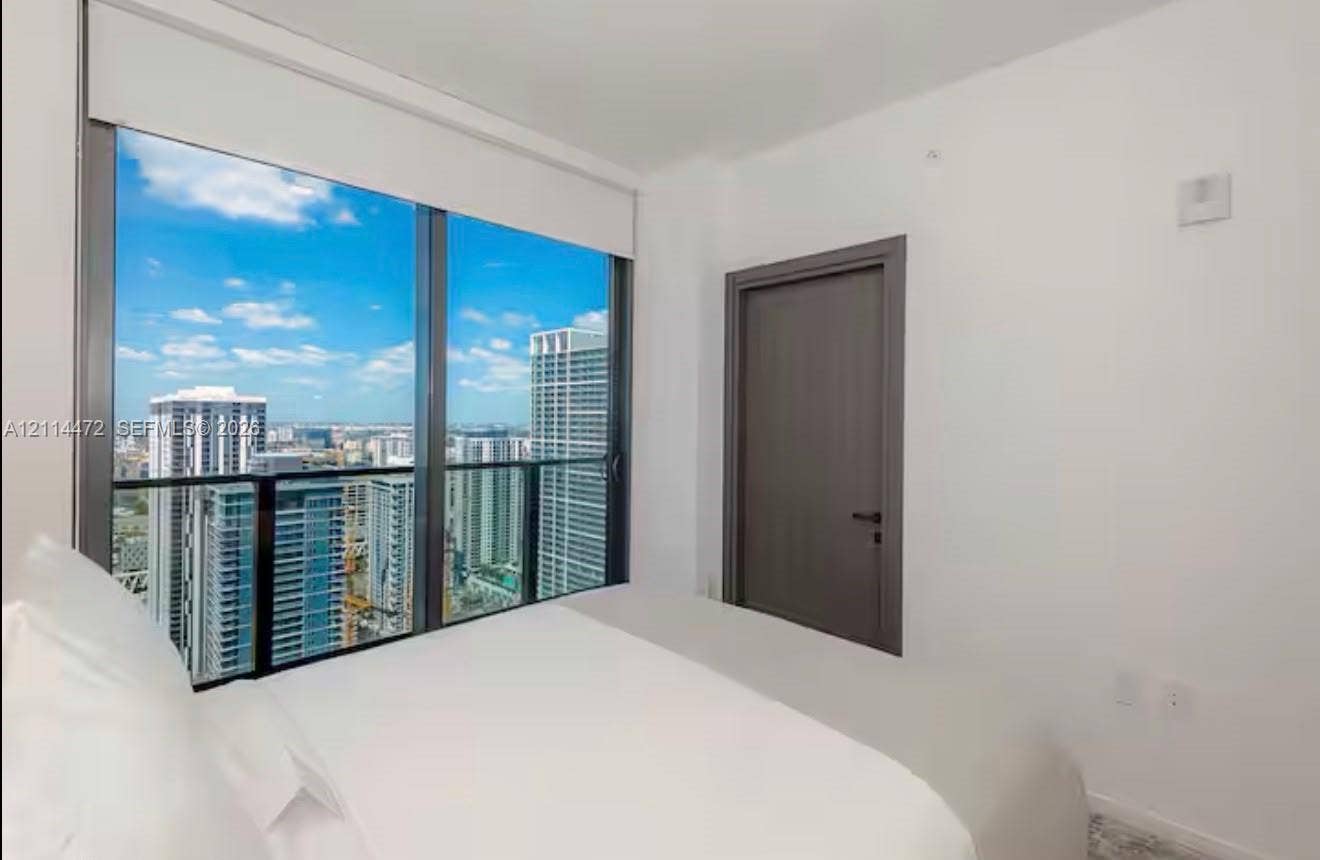 398 NE 5th Street, #4001, Miami, FL 33132 Floor-to-ceiling windows with dark metallic frames, panoramic cityscape, retractable roller shade, and solid-core door with matte black hardware