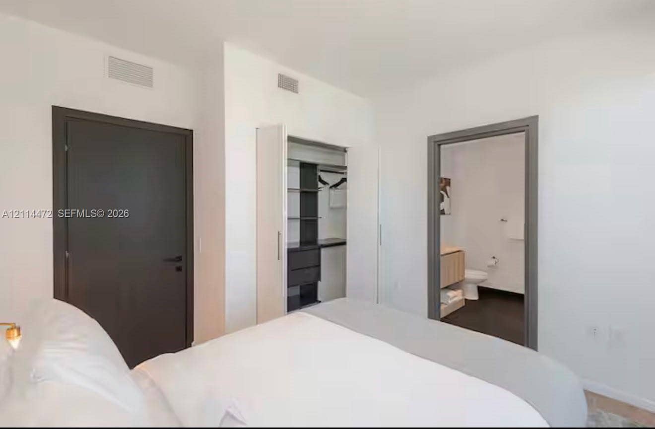 398 NE 5th Street, #4001, Miami, FL 33132 Neutral-toned bedroom featuring a dark solid-core door, built-in closet with integrated shelving, and a doorway showcasing a vanity with a light-finish cabinet