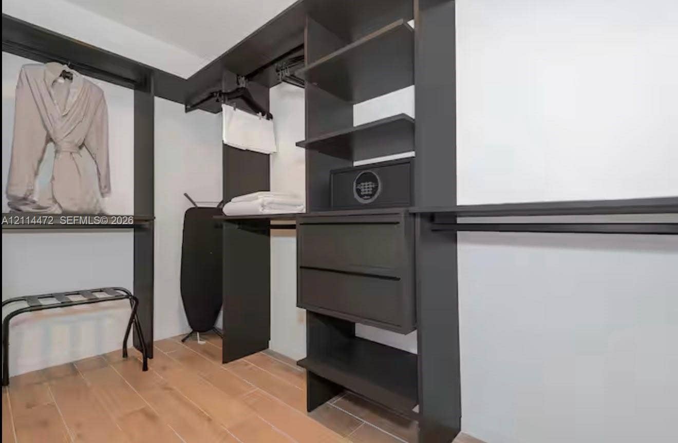 398 NE 5th Street, #4001, Miami, FL 33132 Walk-in closet featuring floor-to-ceiling dark-finish built-in cabinetry, multiple hanging rods, integrated drawer storage, and wood-finish flooring