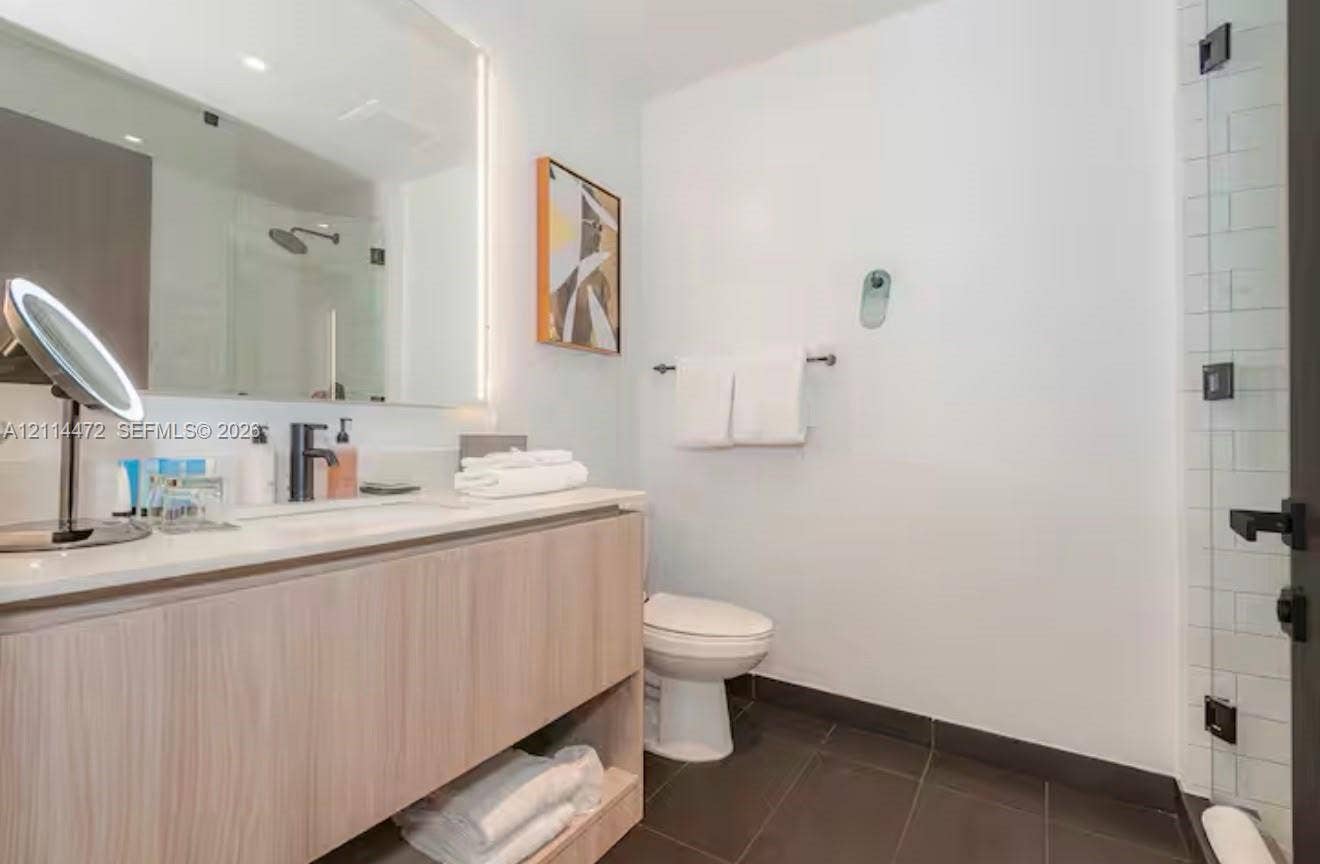 398 NE 5th Street, #4001, Miami, FL 33132 Floating wood-finish vanity with a rectangular sink, integrated LED mirror lighting, dark-toned floor tiling, and a glass-enclosed shower with subway tile surround