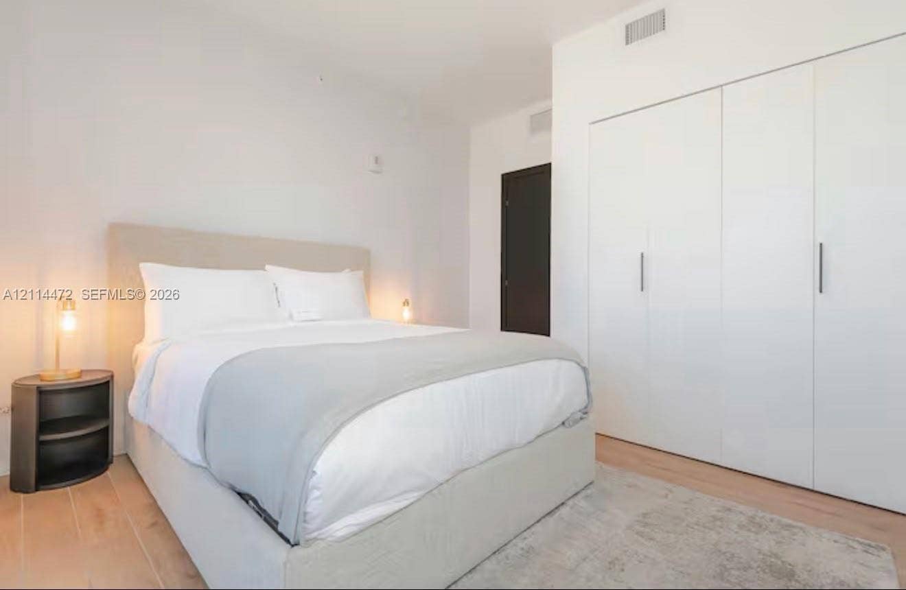 398 NE 5th Street, #4001, Miami, FL 33132 Room featuring smooth-finish white walls, light-toned wood-finish flooring, and built-in floor-to-ceiling storage cabinetry with vertical metallic hardware