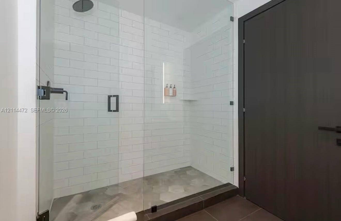 398 NE 5th Street, #4001, Miami, FL 33132 Walk-in shower featuring a frameless glass enclosure, white subway tile surround, hexagonal tile flooring, matte black rainfall showerhead, and integrated recessed shelving
