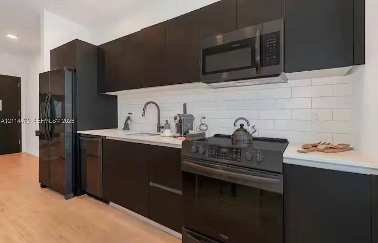 398 NE 5th Street, #4001, Miami, FL 33132 Modern kitchen featuring matte black flat-panel cabinetry, white solid surface countertops, white subway tile backsplash, and a suite of black appliances