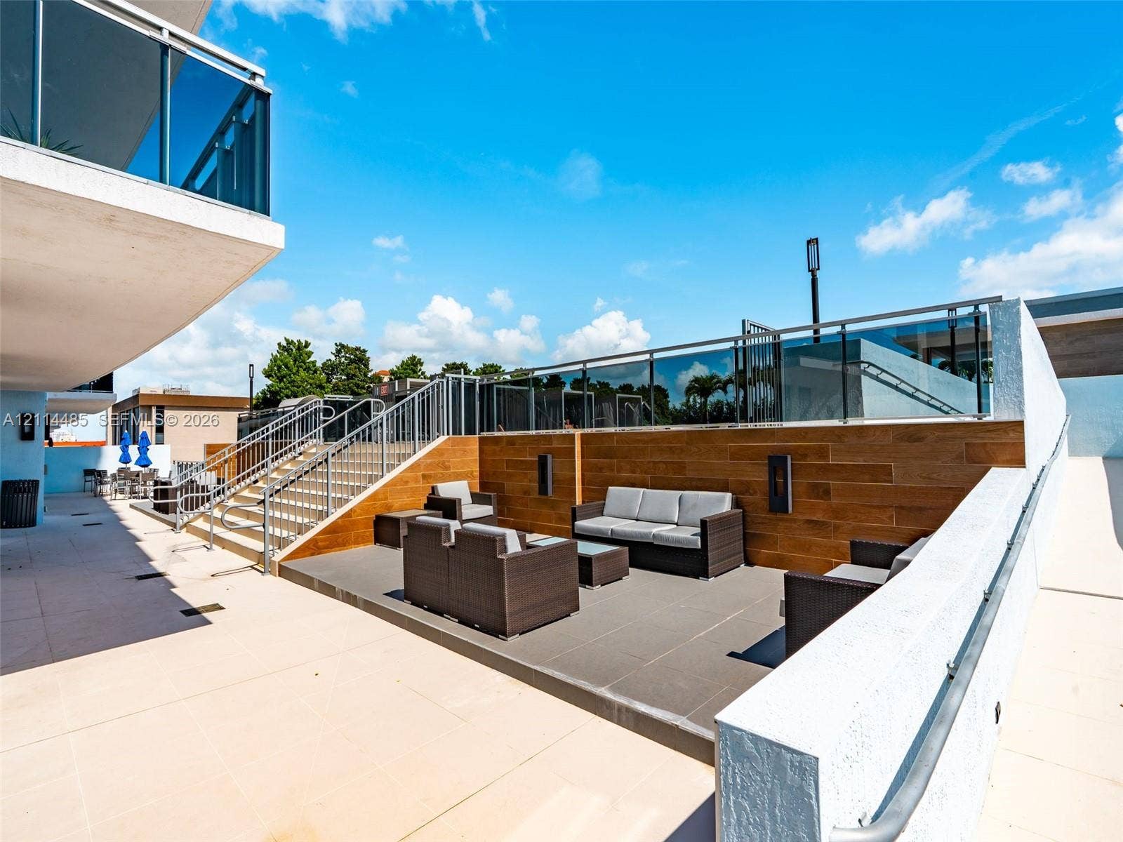Multi-level terrace featuring tile flooring, wood-finish wall paneling, stainless steel railings with glass inserts, and tiered staircases