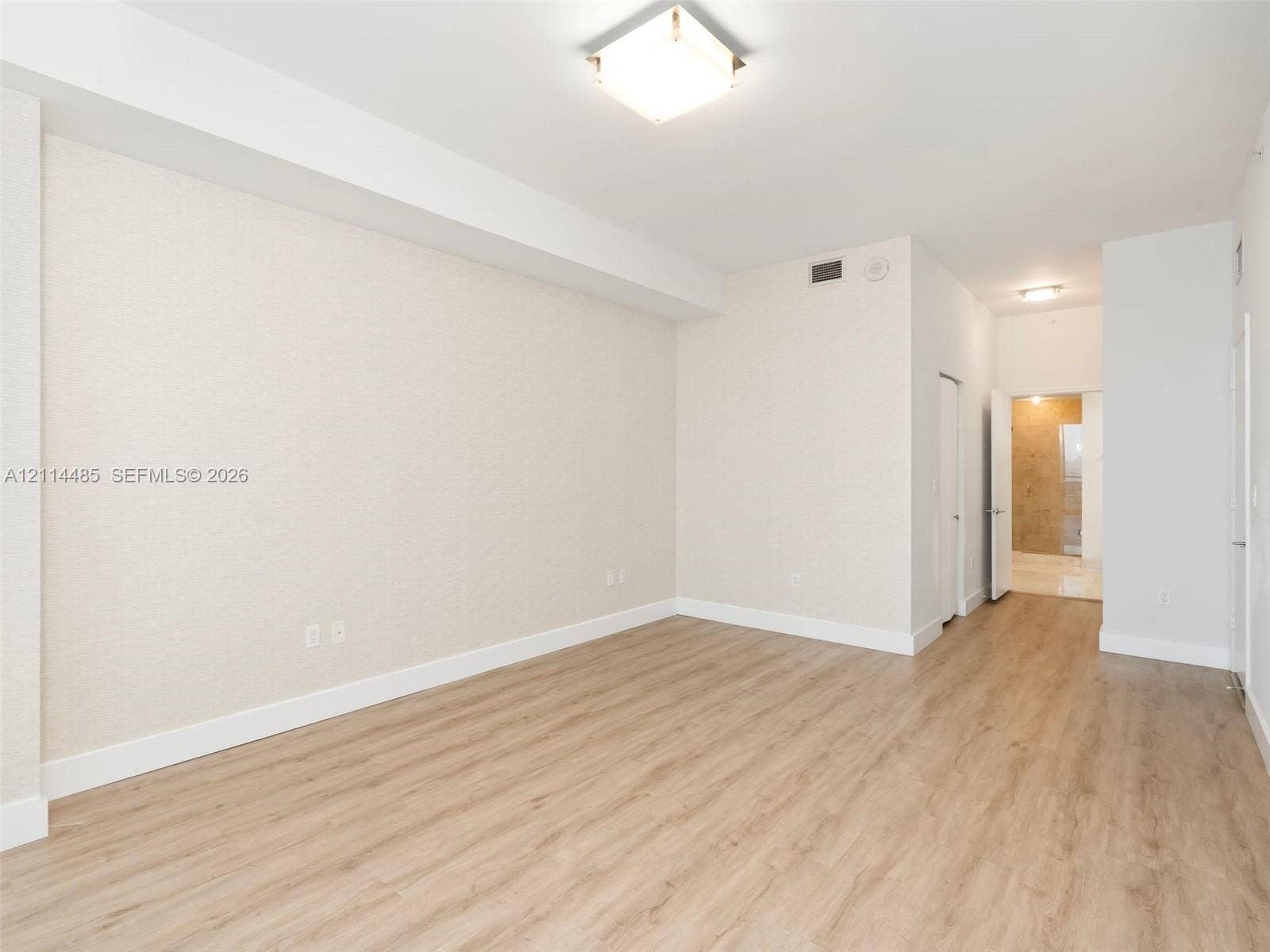 Neutral-toned interior space featuring wood-finish flooring, textured wall finishes, and a flush-mount square ceiling light fixture