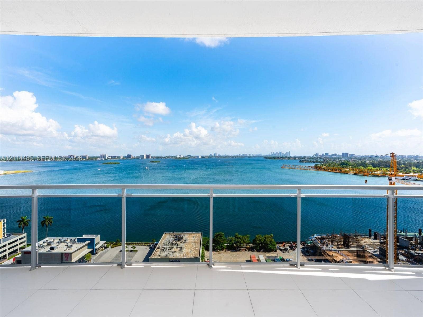 Covered balcony featuring expansive water frontage, large-format tile flooring, and a minimalist glass-panel railing