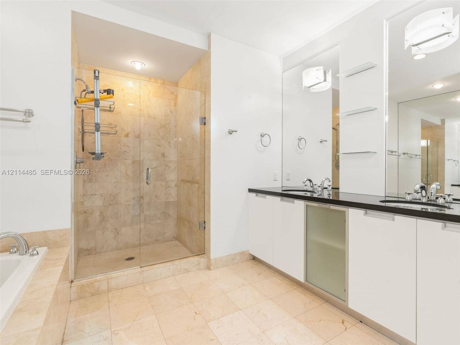 Walk-in shower with stone tile enclosure, dual-sink vanity with dark countertop, large wall-mounted mirrors, and built-in glass shelving