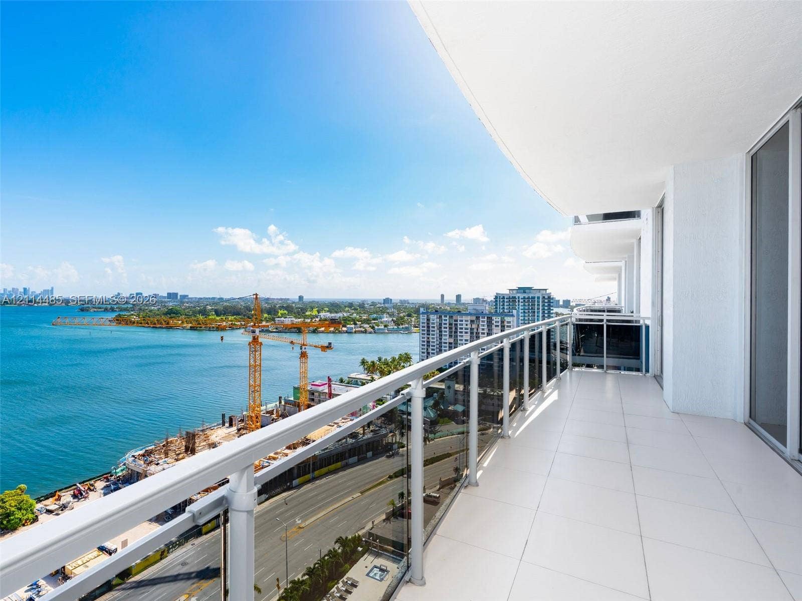 Covered balcony featuring white tile flooring, glass and metal railing, and expansive water backdrop