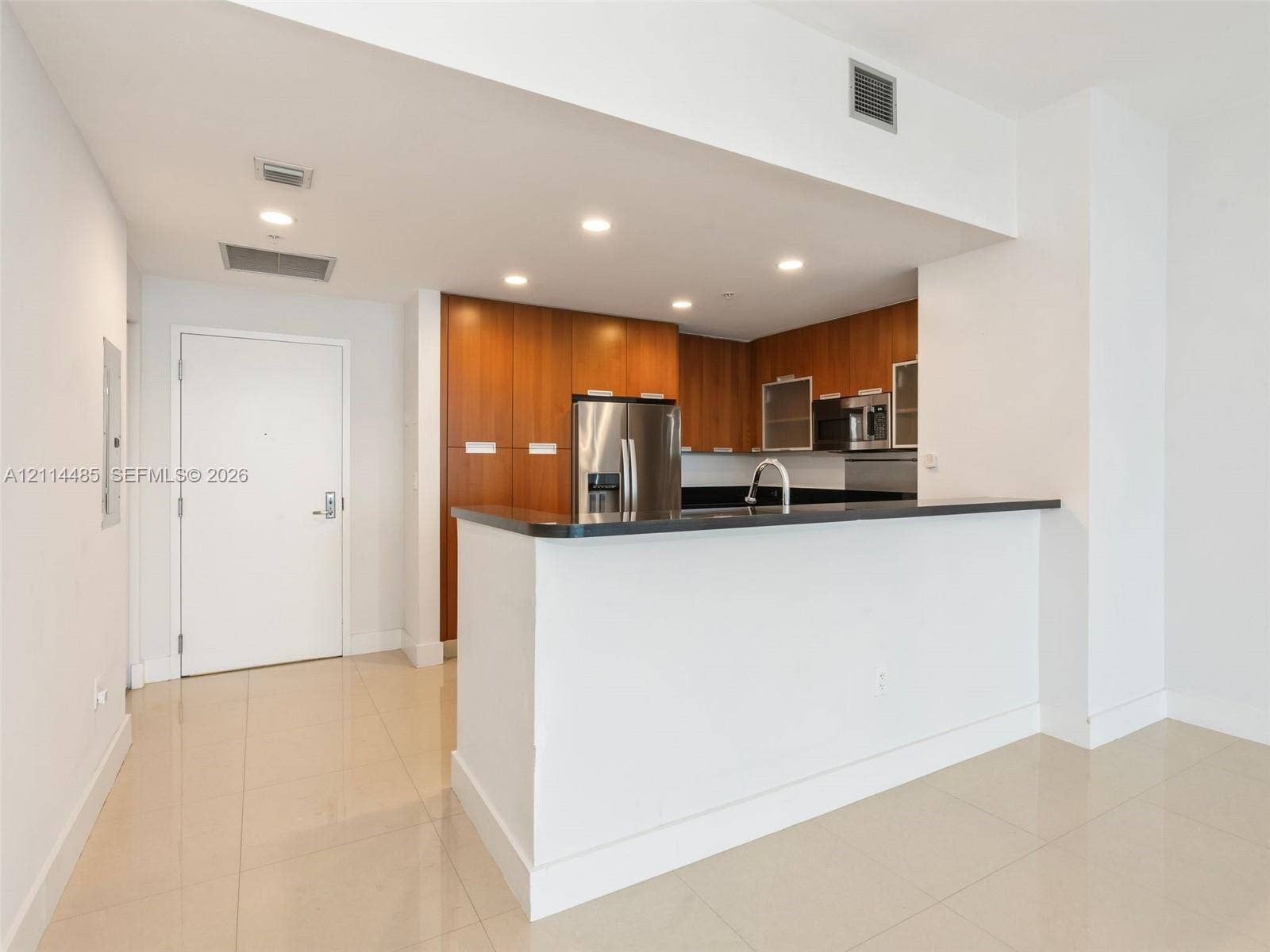 Kitchen featuring wood-finish cabinetry, dark solid-surface countertops, stainless steel appliances, a peninsula counter, and tile flooring