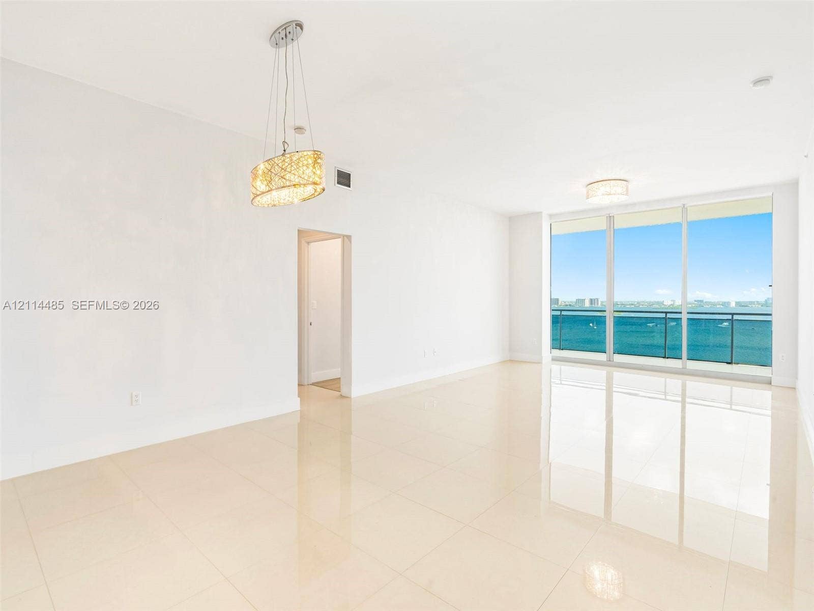 Open-concept room featuring polished tile flooring, floor-to-ceiling glass windows, a balcony with a glass railing, and decorative pendant lighting