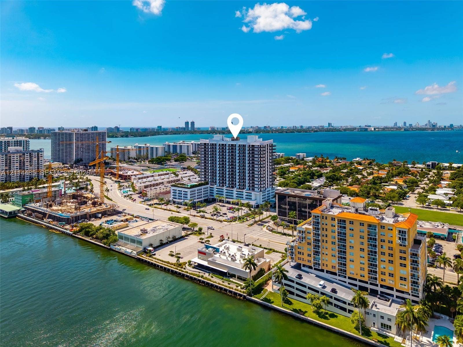 Aerial perspective of a high-rise residential building featuring expansive water frontage, proximity to the coastline, and surrounding urban infrastructure