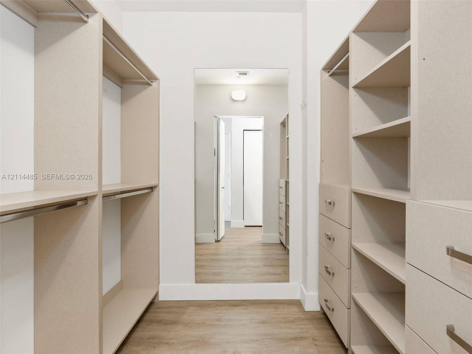 Walk-in closet featuring custom built-in cabinetry, floor-to-ceiling shelving, integrated storage drawers with brushed metal hardware, and wood-finish flooring