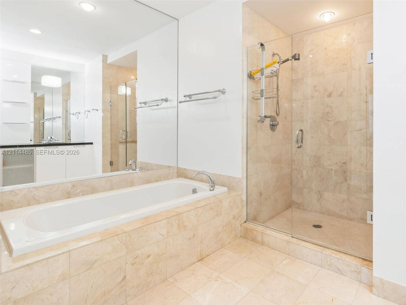 Bathroom featuring a tiled soaking tub, separate glass-enclosed shower, expansive wall-to-wall mirror, built-in cabinetry with a countertop, and recessed lighting