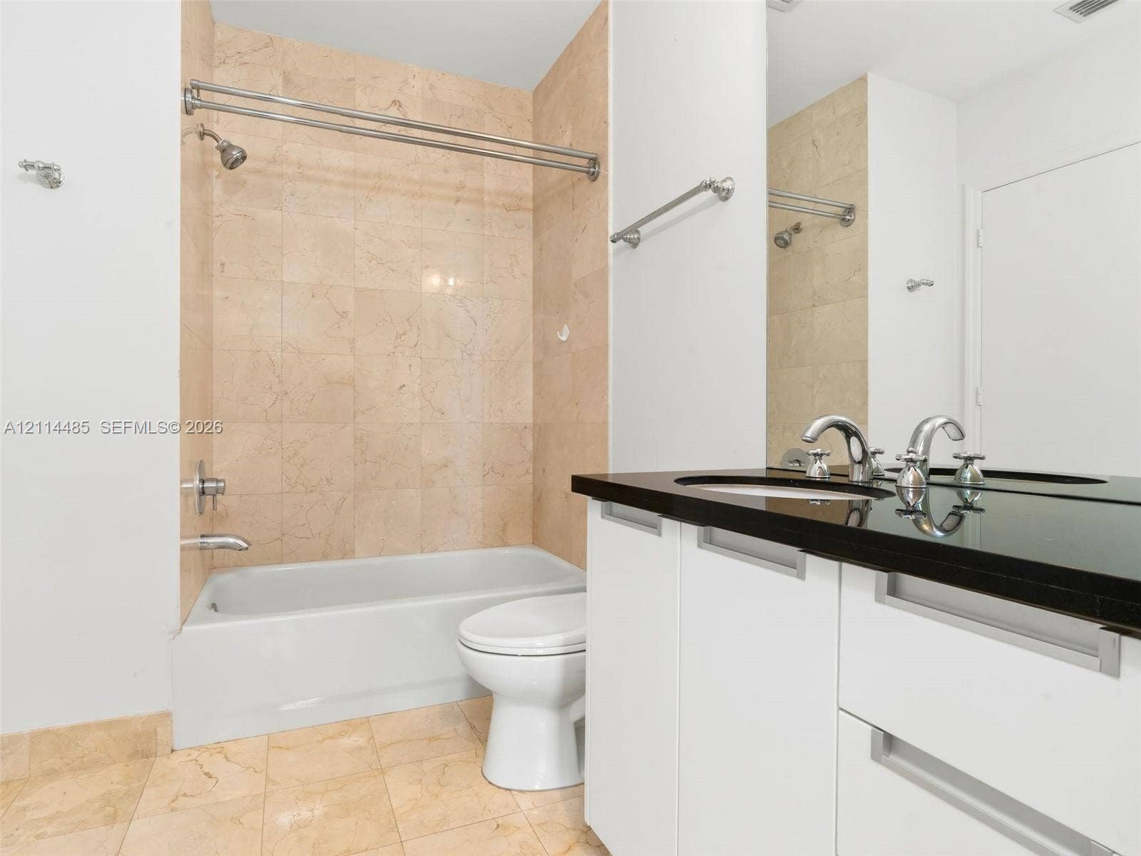 Bathroom featuring a vanity with dark stone countertop, white flat-panel cabinetry with integrated pulls, tile flooring, and a tub-shower combination with floor-to-ceiling stone-finish tile surround