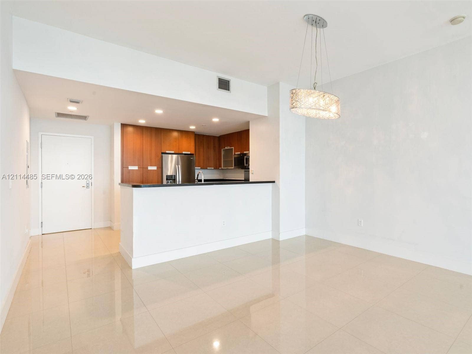 Kitchen featuring wood-finish cabinetry, a breakfast bar with stone-surface countertop, stainless steel appliances, polished tile flooring, and a decorative pendant light fixture
