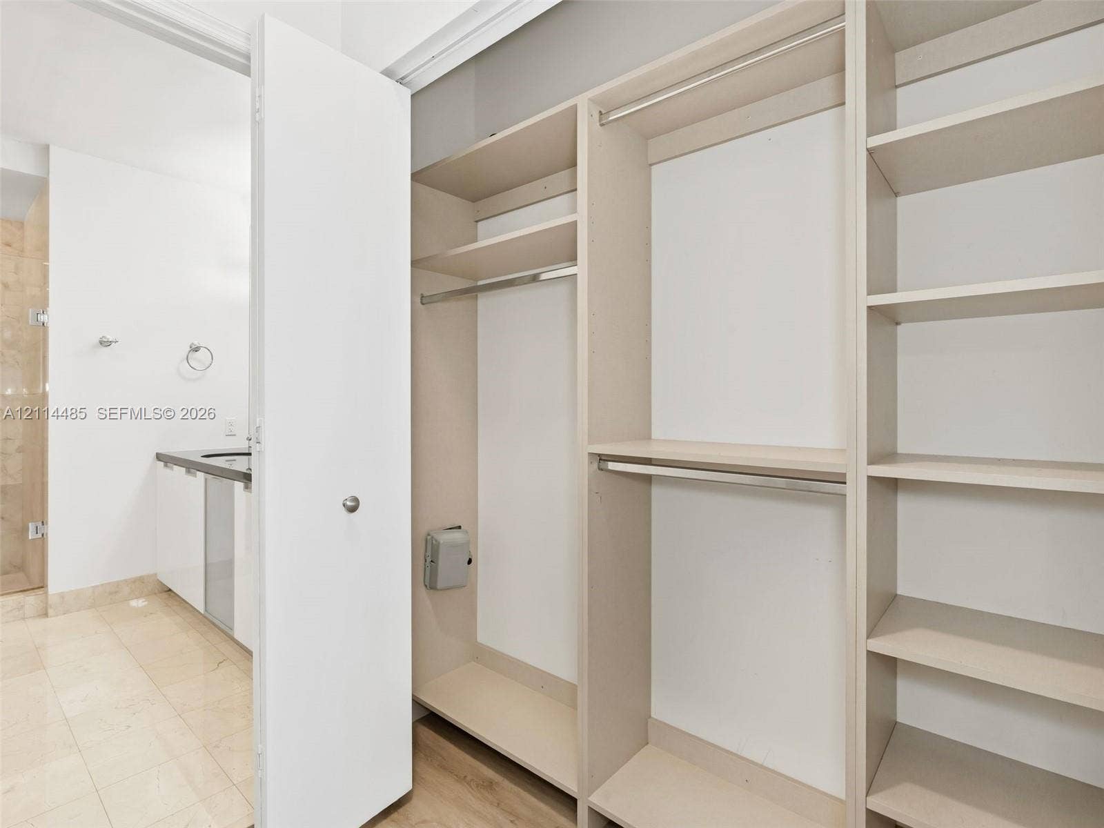 Custom walk-in closet featuring built-in shelving and dual metal hanging rods, paired with a bathroom containing a stone-surfaced vanity and tiled flooring