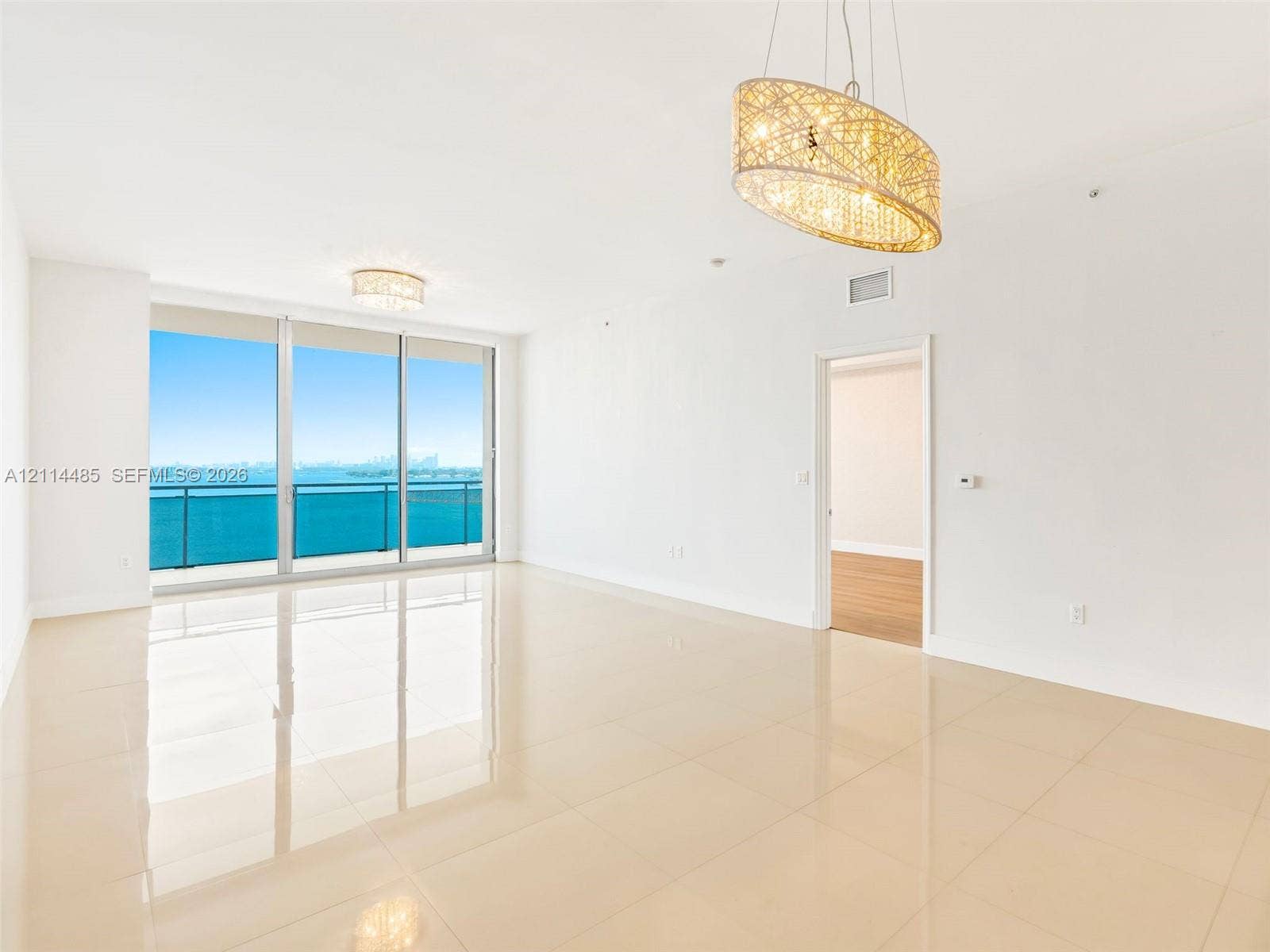 Open-concept interior featuring large-format tile flooring, floor-to-ceiling glass sliding doors, a metal-framed balcony, and dual decorative pendant light fixtures