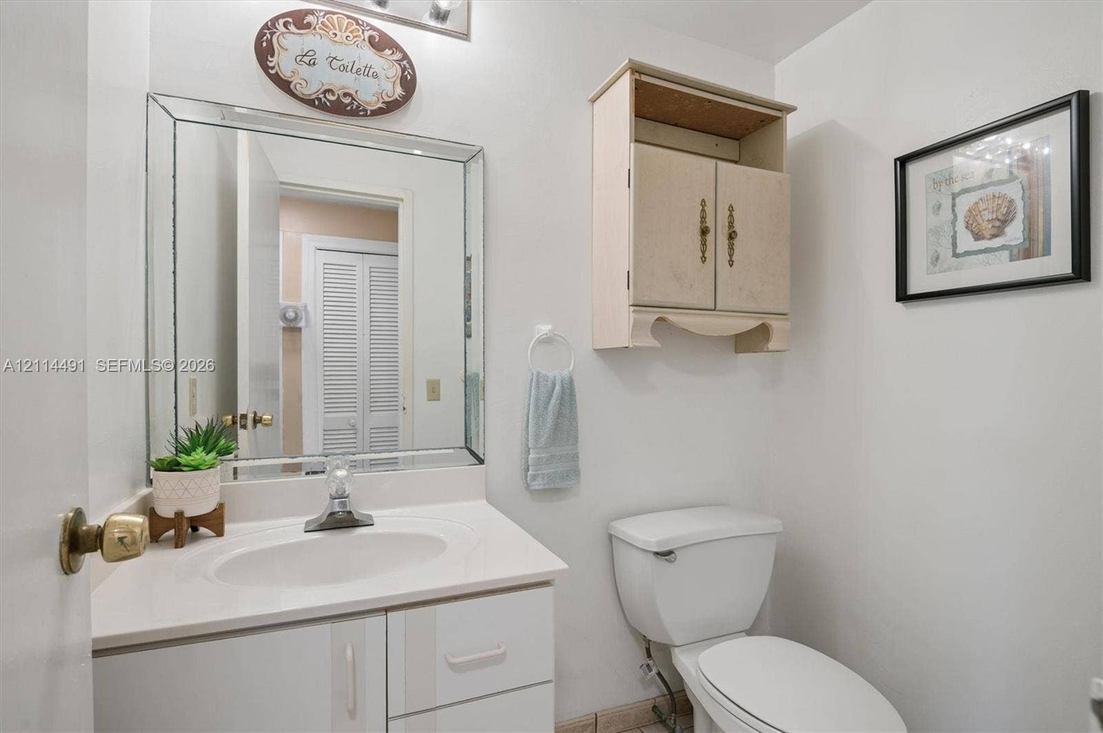 3505 S Ocean Drive, #217, Hollywood, FL 33019 Bathroom featuring a white vanity cabinet with a stone-finish countertop, an oval undermount sink, a beveled-edge wall mirror, and a wall-mounted wooden storage cabinet