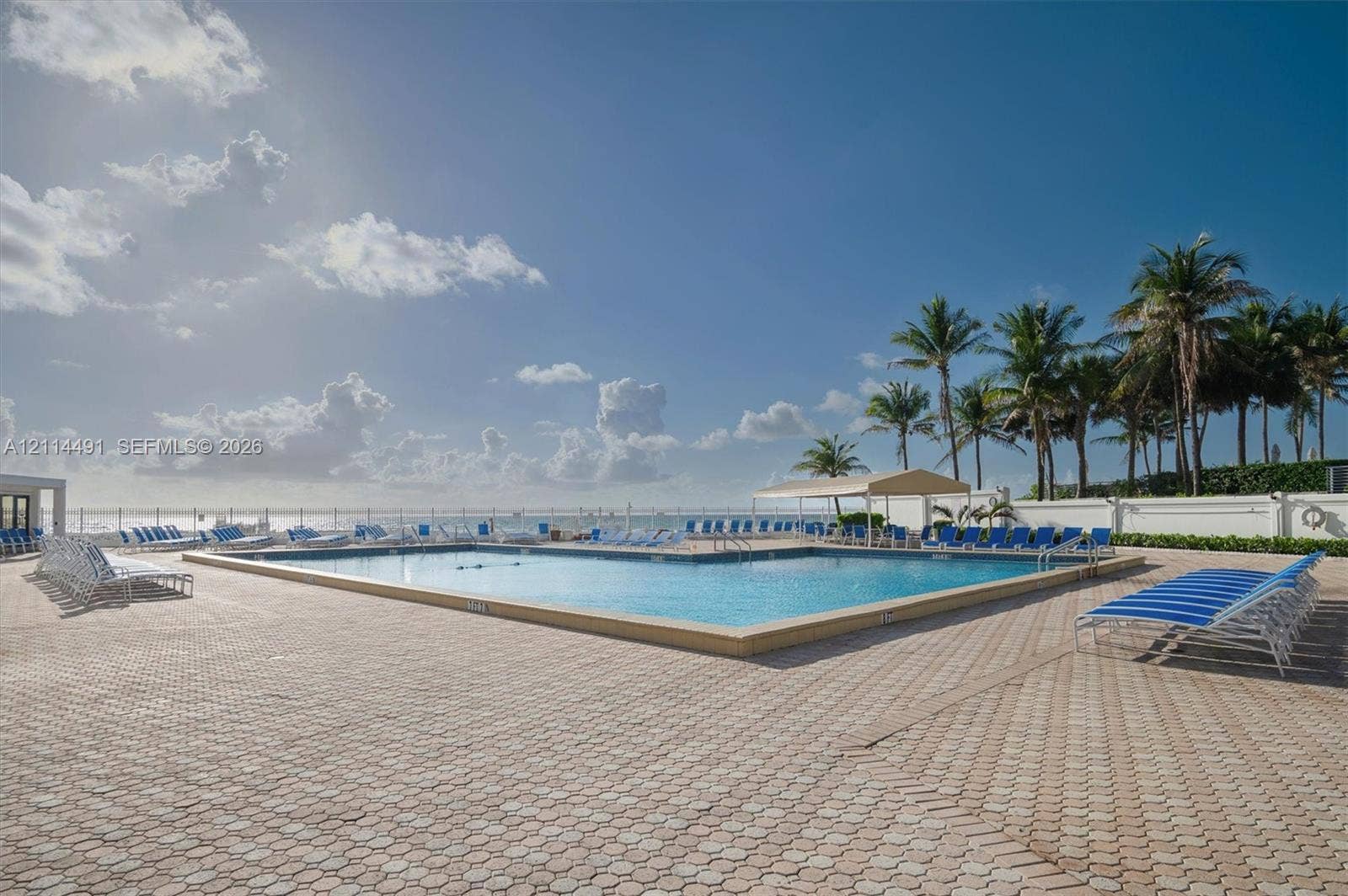3505 S Ocean Drive, #217, Hollywood, FL 33019 In-ground swimming pool featuring a geometric design, expansive paved patio, permanent shade structure, and perimeter fencing