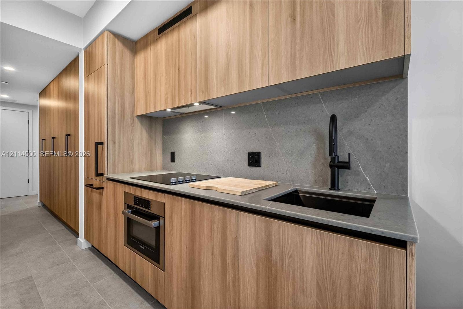 121 NE 5th Street, #712B, Miami, FL 33132 Kitchen featuring wood-finish cabinetry, stone slab backsplash, quartz countertops, undermount sink with matte black faucet, and built-in stainless steel appliances