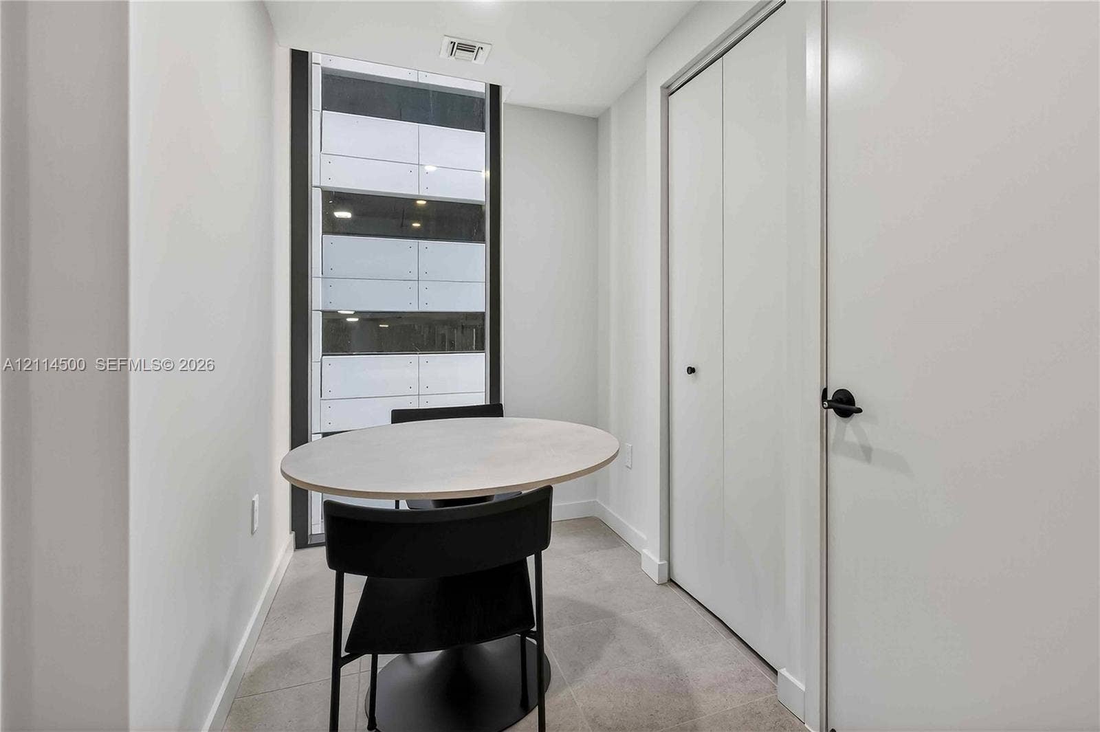 121 NE 5th Street, #712B, Miami, FL 33132 Neutral-toned interior space featuring large floor-to-ceiling windows, tile flooring, and white double-door closet storage with matte black hardware