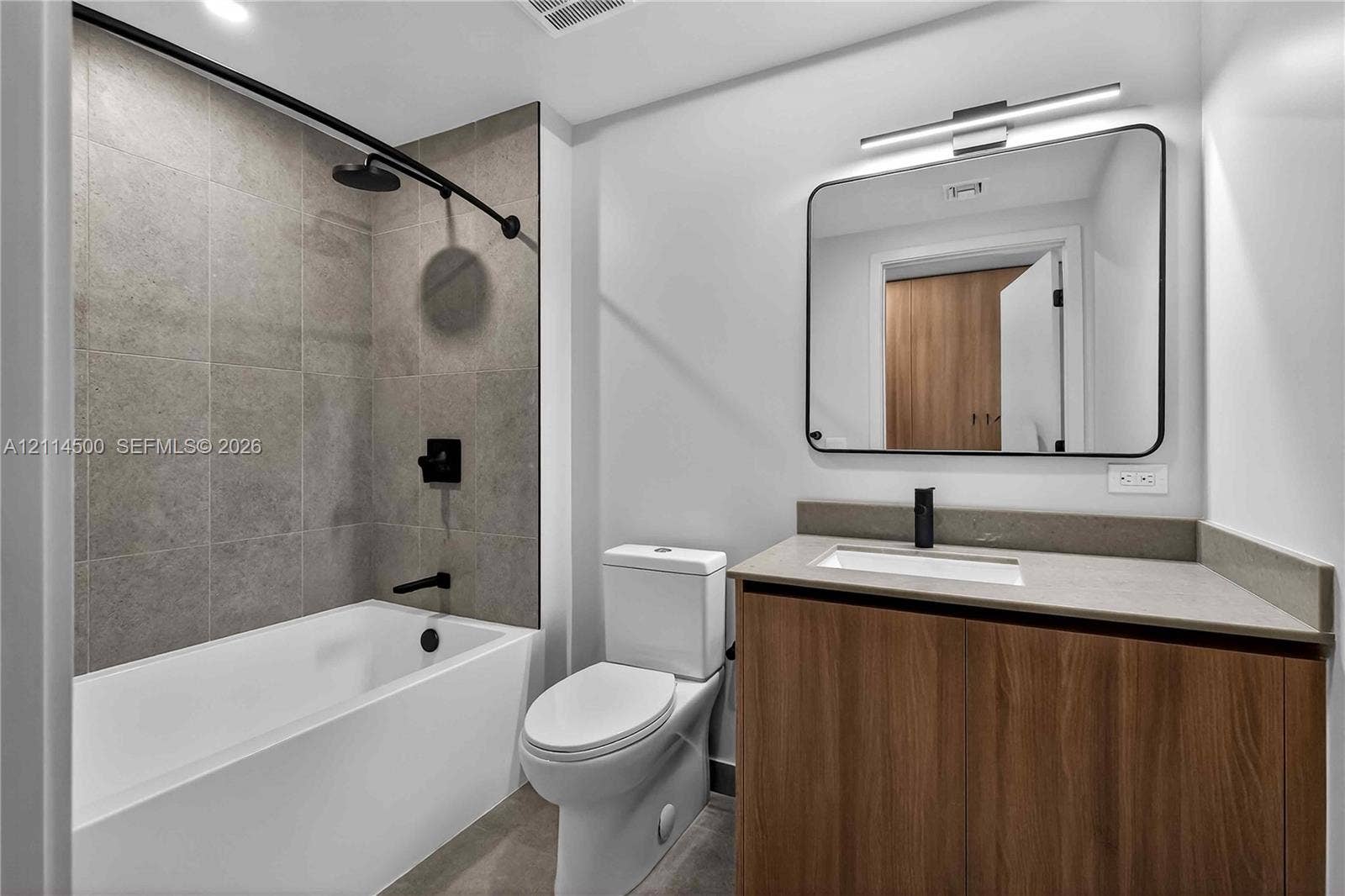 121 NE 5th Street, #712B, Miami, FL 33132 Bathroom featuring a wood-finish vanity with a stone-composite countertop, matte black fixtures, a rectangular undermount sink, and a tiled shower surround