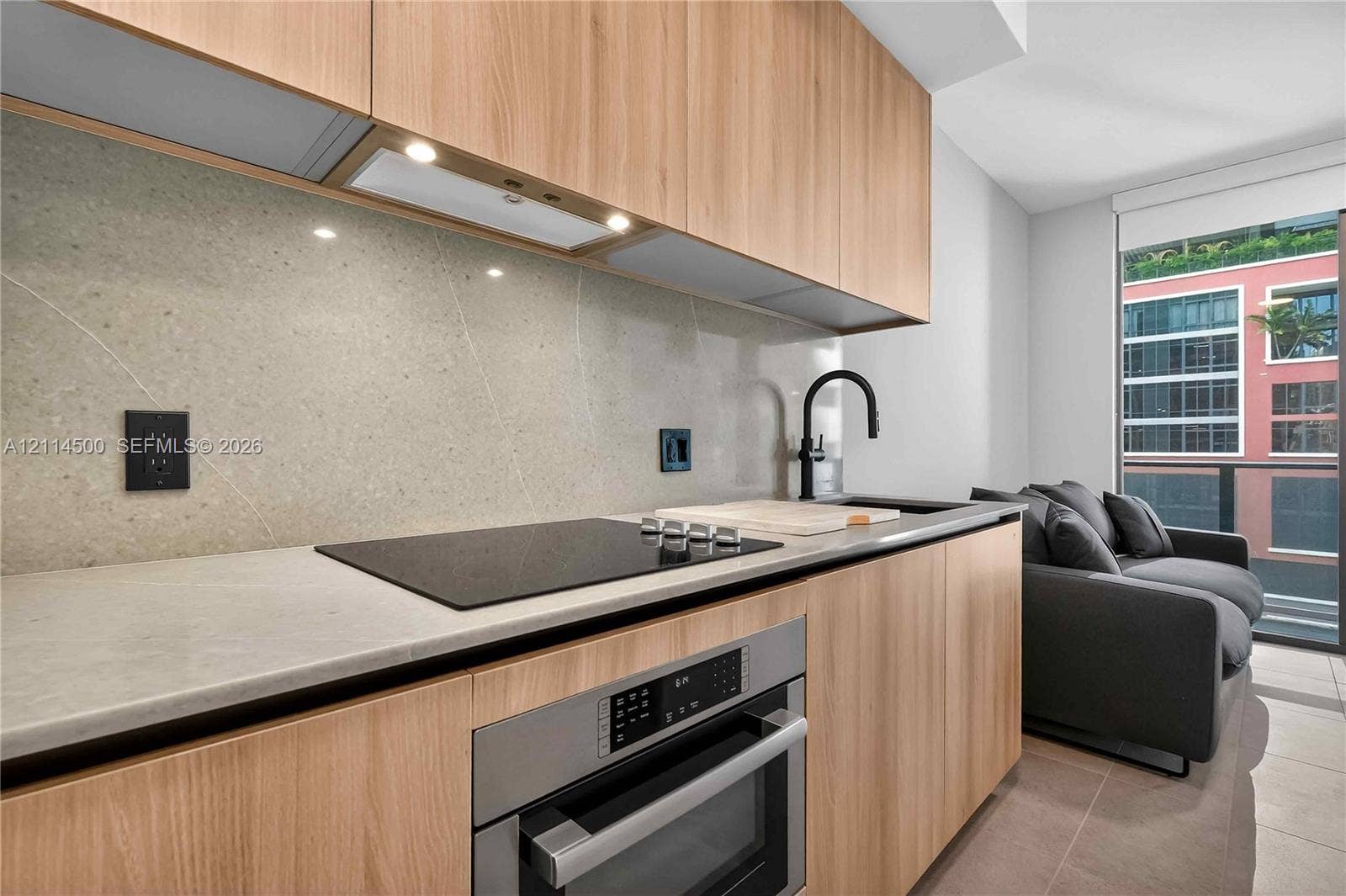 121 NE 5th Street, #712B, Miami, FL 33132 Kitchen featuring light wood-finish cabinetry, stone slab backsplash, integrated induction cooktop, built-in stainless steel oven, and matte black faucet