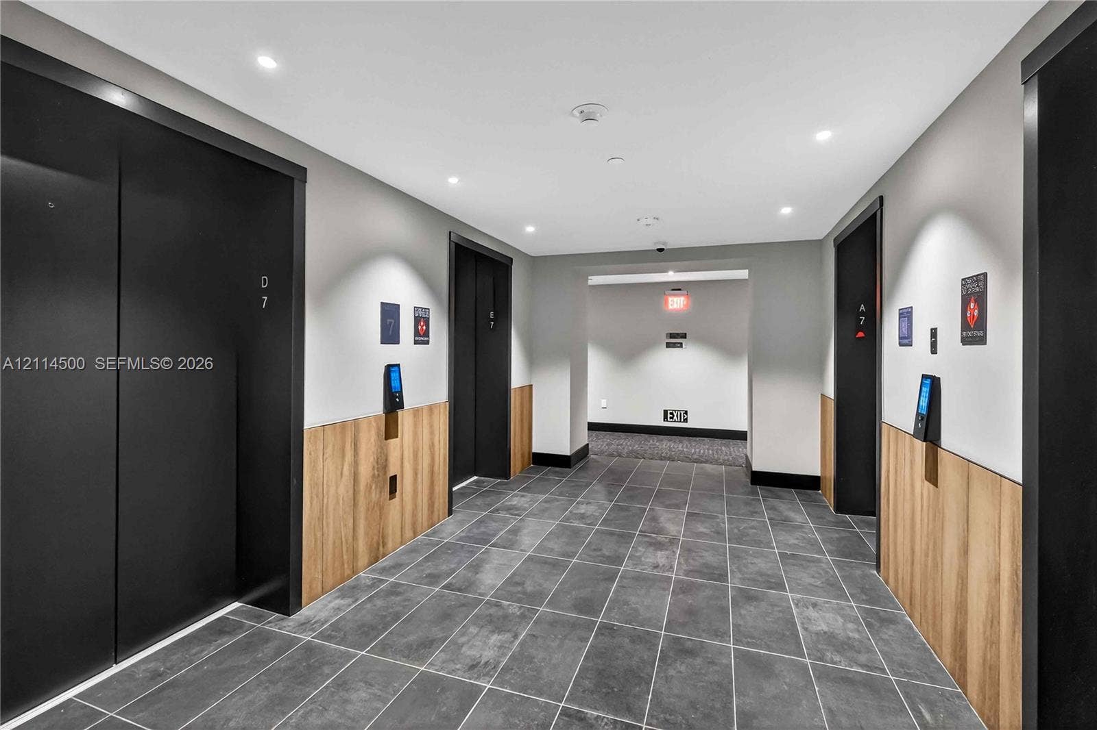 121 NE 5th Street, #712B, Miami, FL 33132 Elevator lobby featuring matte black doors, wood-finish lower wall paneling, large-format tile flooring, and recessed ceiling lighting