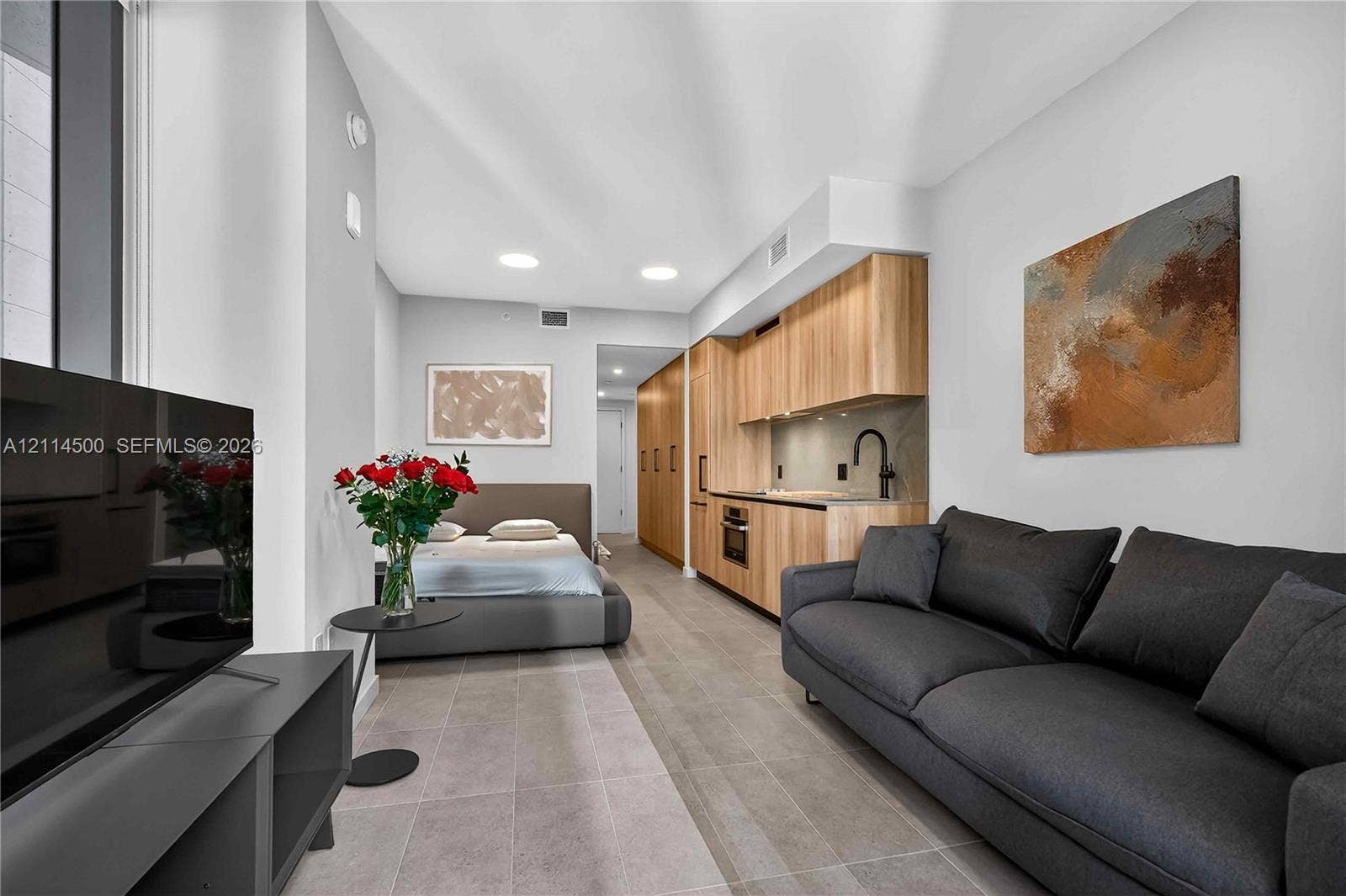 121 NE 5th Street, #712B, Miami, FL 33132 Studio interior featuring wood-finish cabinetry, stone-style tile flooring, recessed ceiling lighting, and a built-in kitchen area with a matte black faucet