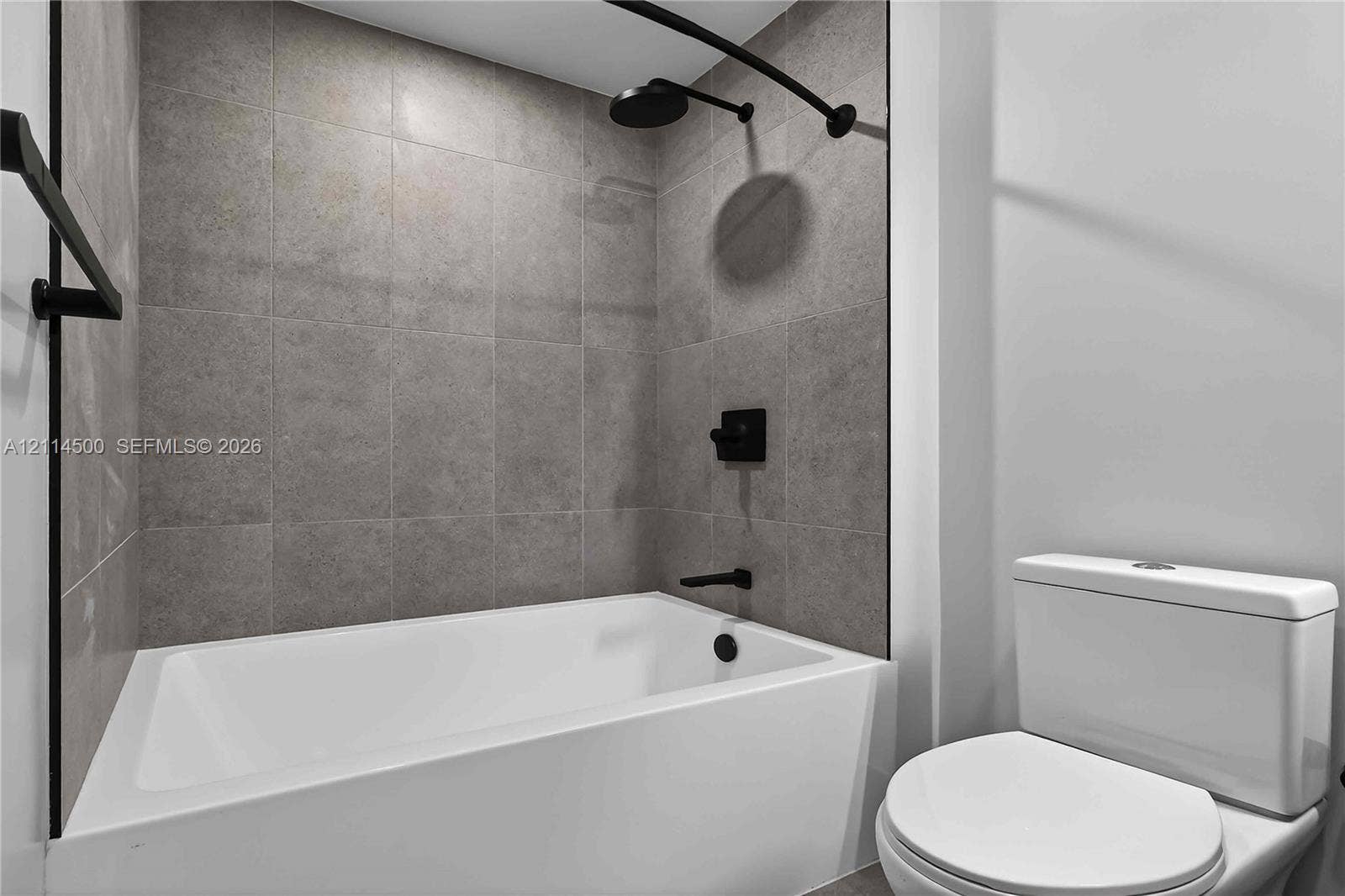 121 NE 5th Street, #712B, Miami, FL 33132 Bathroom featuring a white deep-basin tub, matte black shower head and faucet hardware, and full-height grey tile wall surround