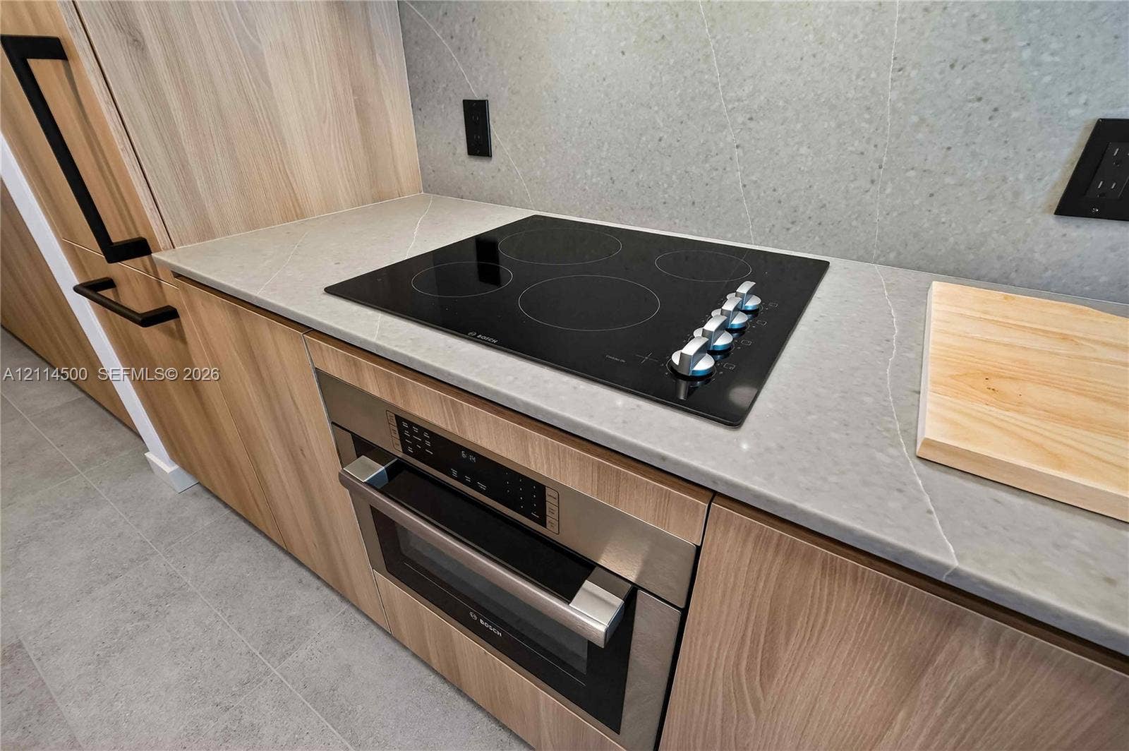 121 NE 5th Street, #712B, Miami, FL 33132 Modern kitchen area featuring flat-panel wood-finish cabinetry, stone-surface countertops, full-height stone backsplash, integrated stainless steel oven, and a black glass electric cooktop