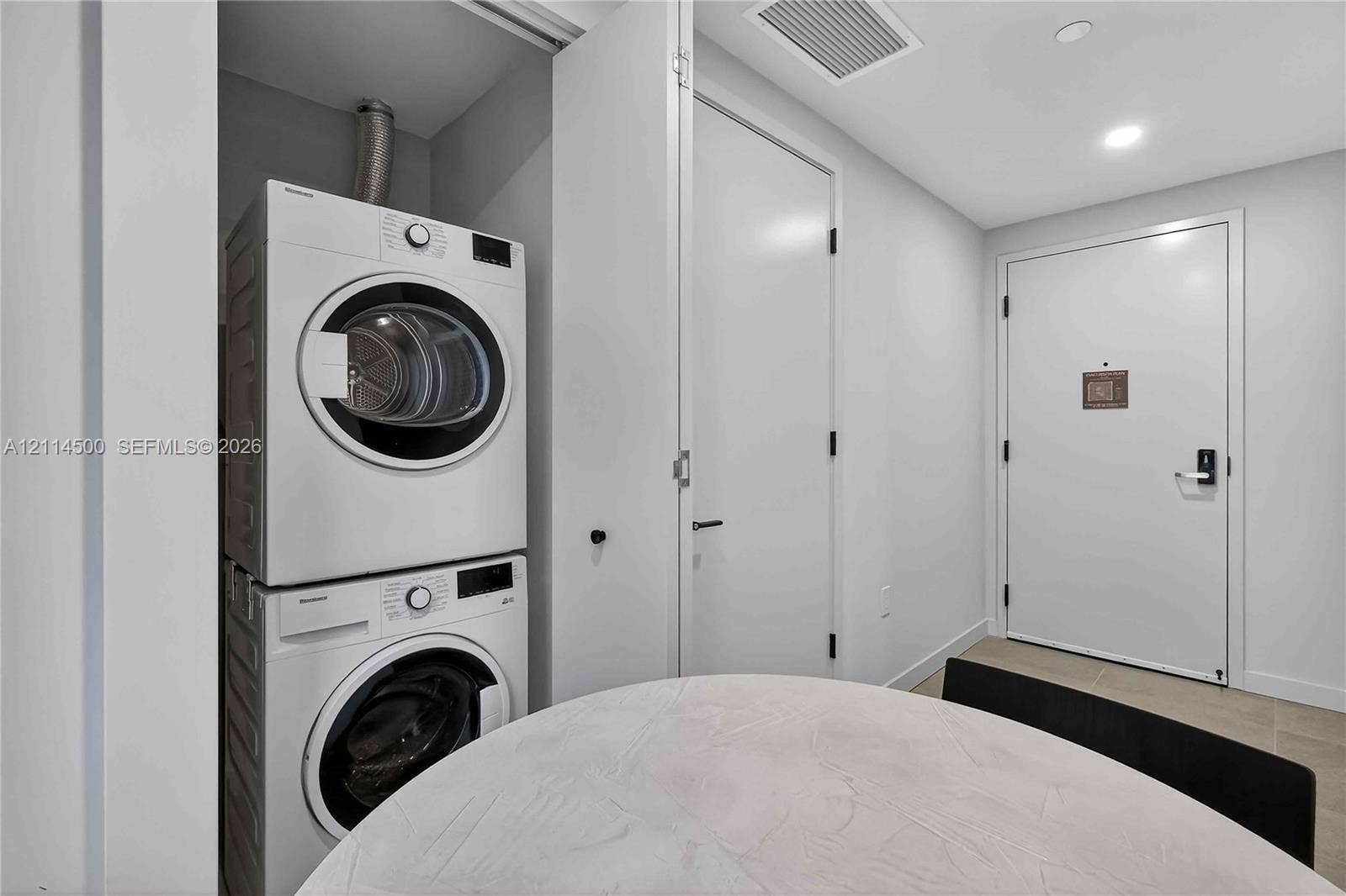 121 NE 5th Street, #712B, Miami, FL 33132 Utility area featuring stacked white laundry appliances, recessed lighting, and a white interior door with metallic hardware