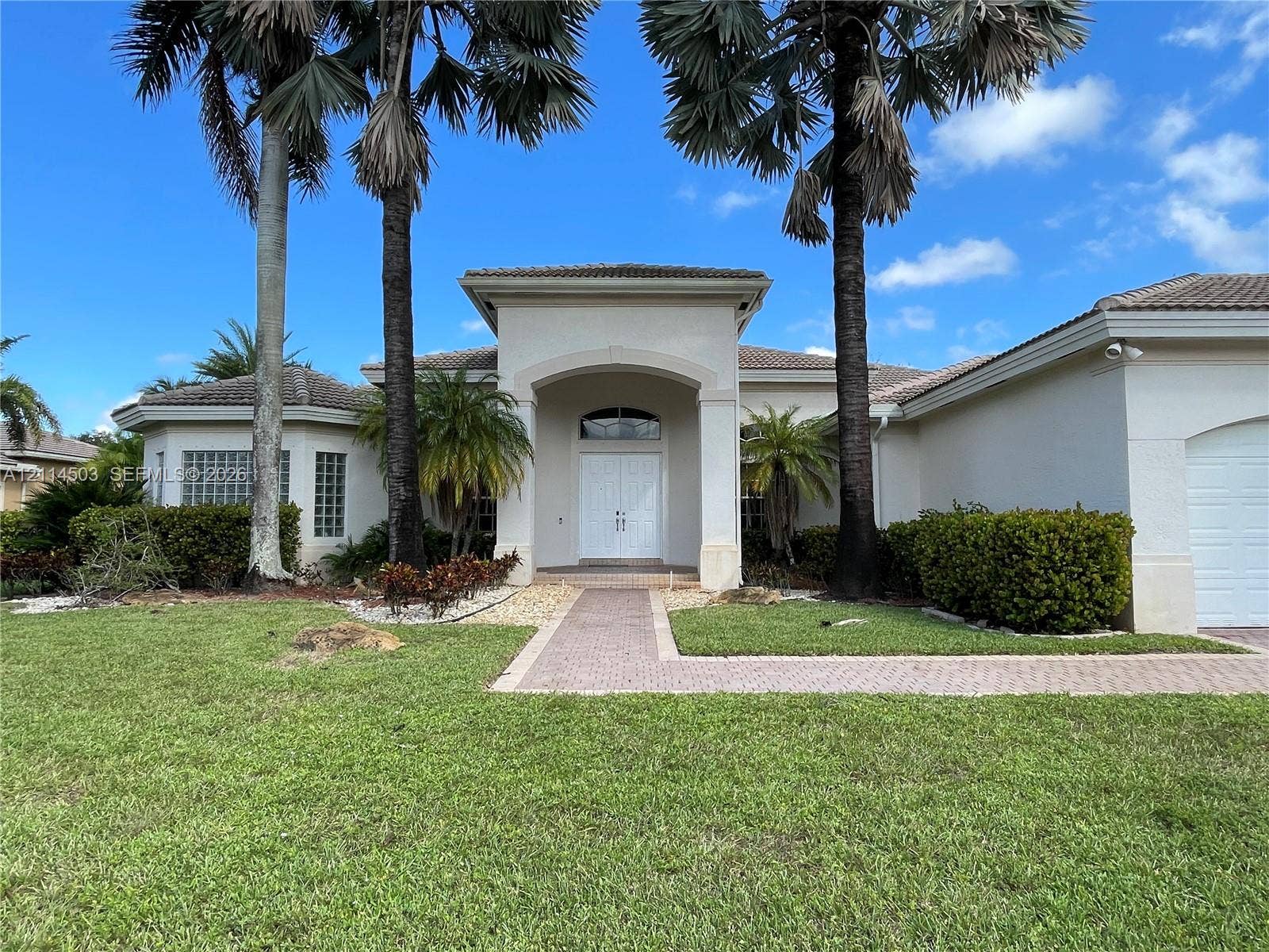 15001 SW 33rd Street, Davie, FL 33331 Stucco exterior featuring a covered entryway with double doors, an arched transom window, glass block window accents, and a paved walkway