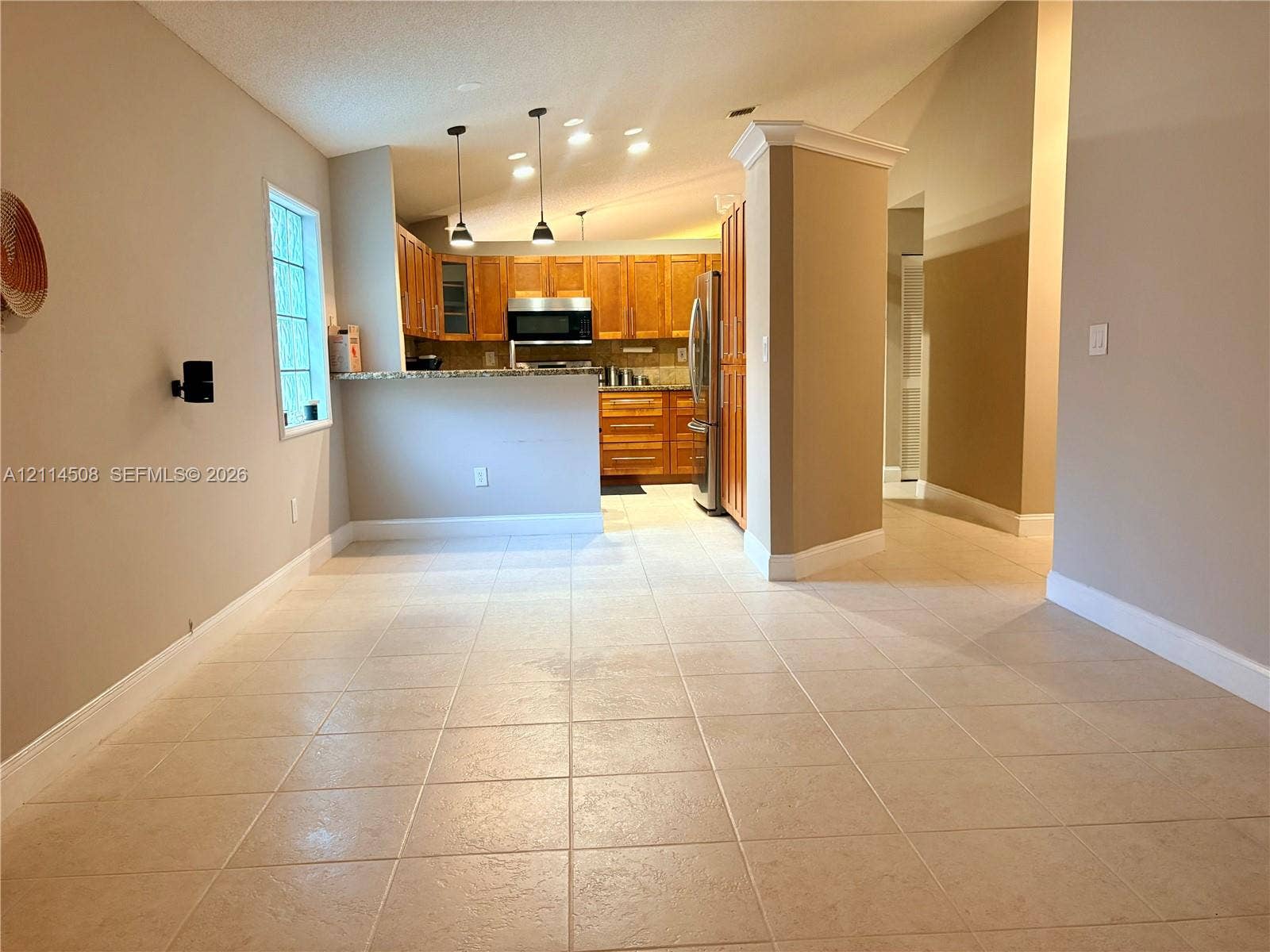Kitchen featuring natural-finish wood cabinetry, stone countertops, stainless steel appliances, breakfast bar with pendant lighting, and ceramic tile flooring