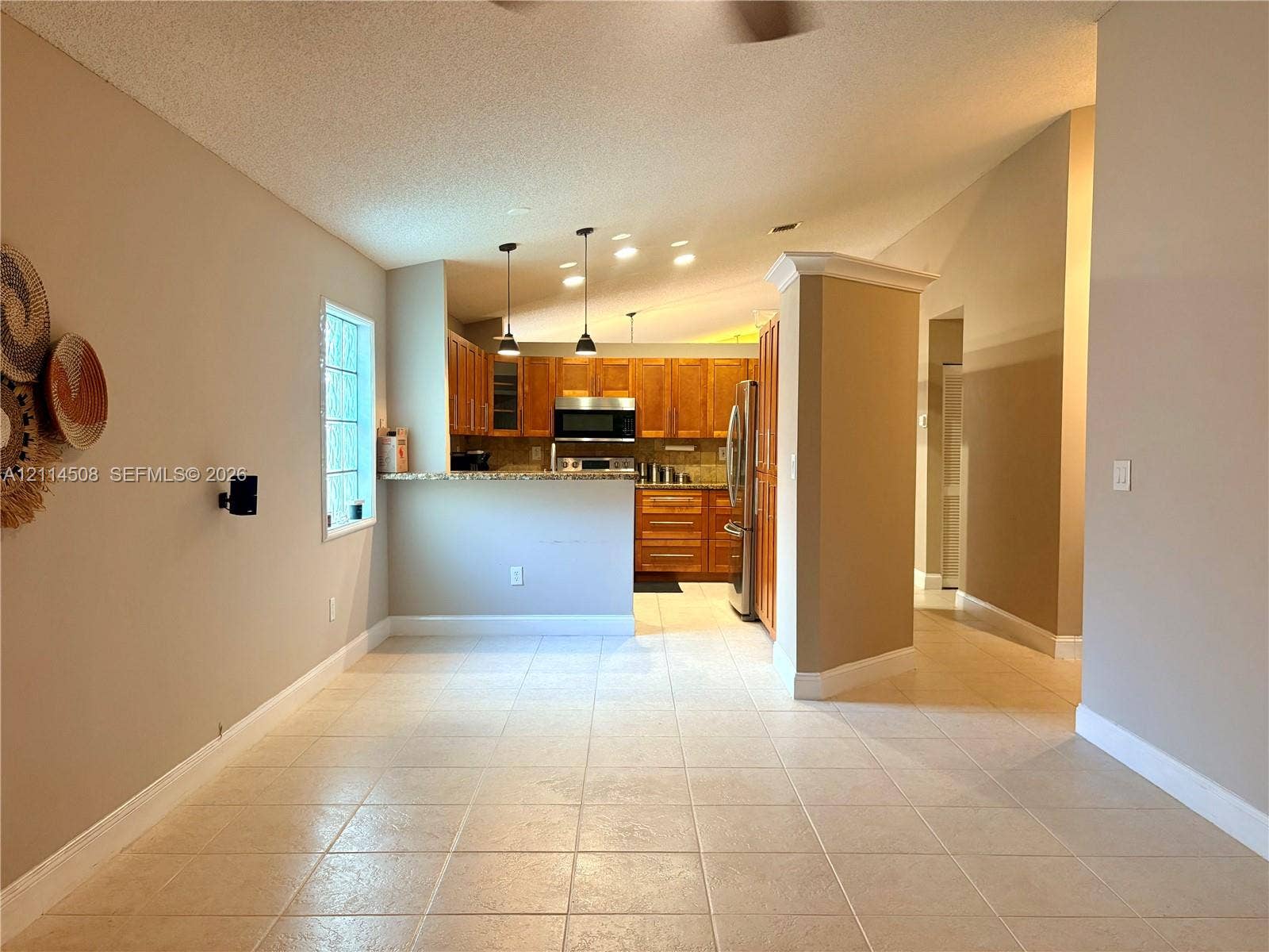 Kitchen featuring wood cabinetry, stone countertops, stainless steel appliances, pendant lighting, and tile flooring