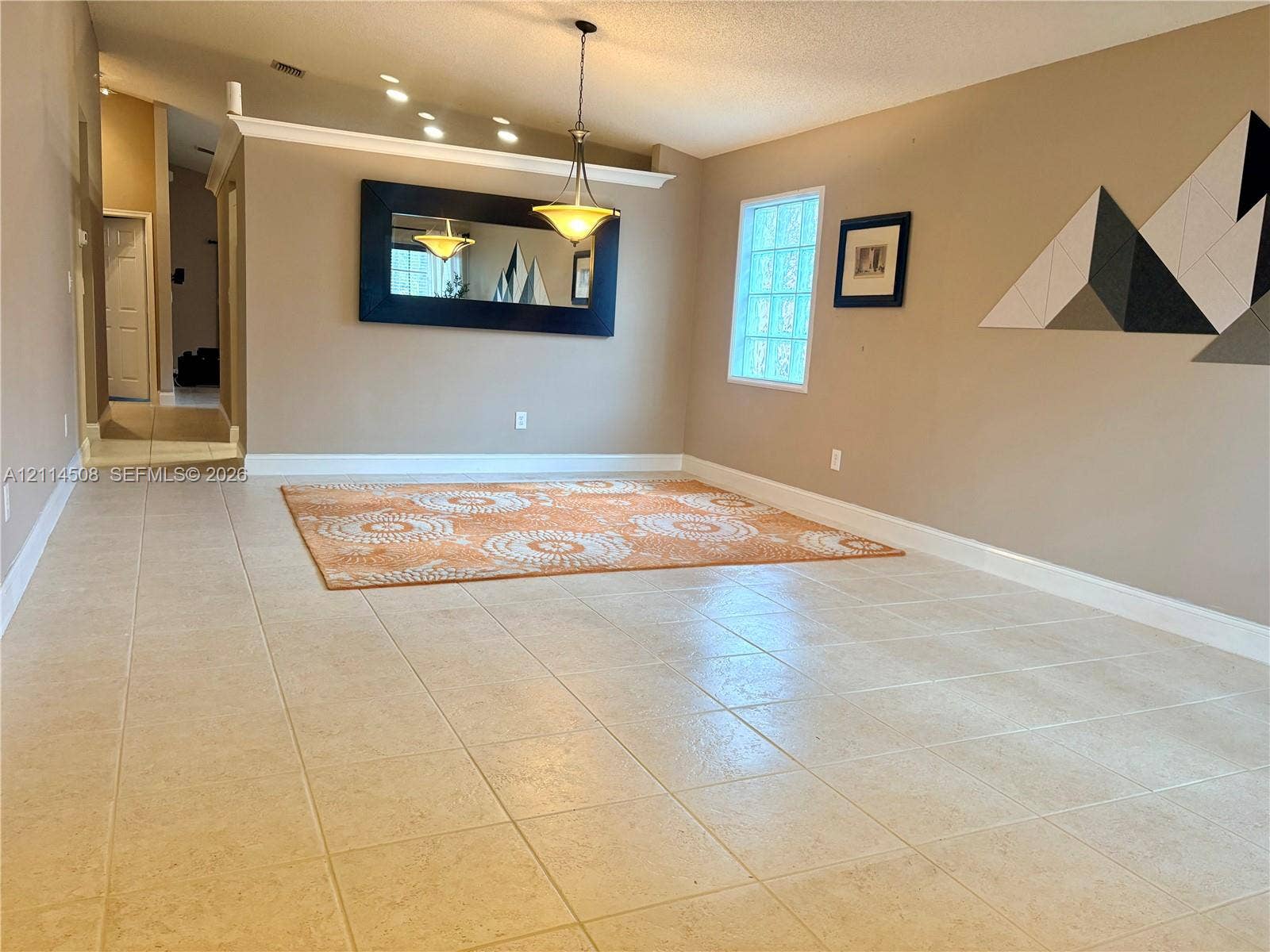 Open-concept area featuring high ceilings, large-format tile flooring, glass block window, and an adjustable pendant lighting fixture