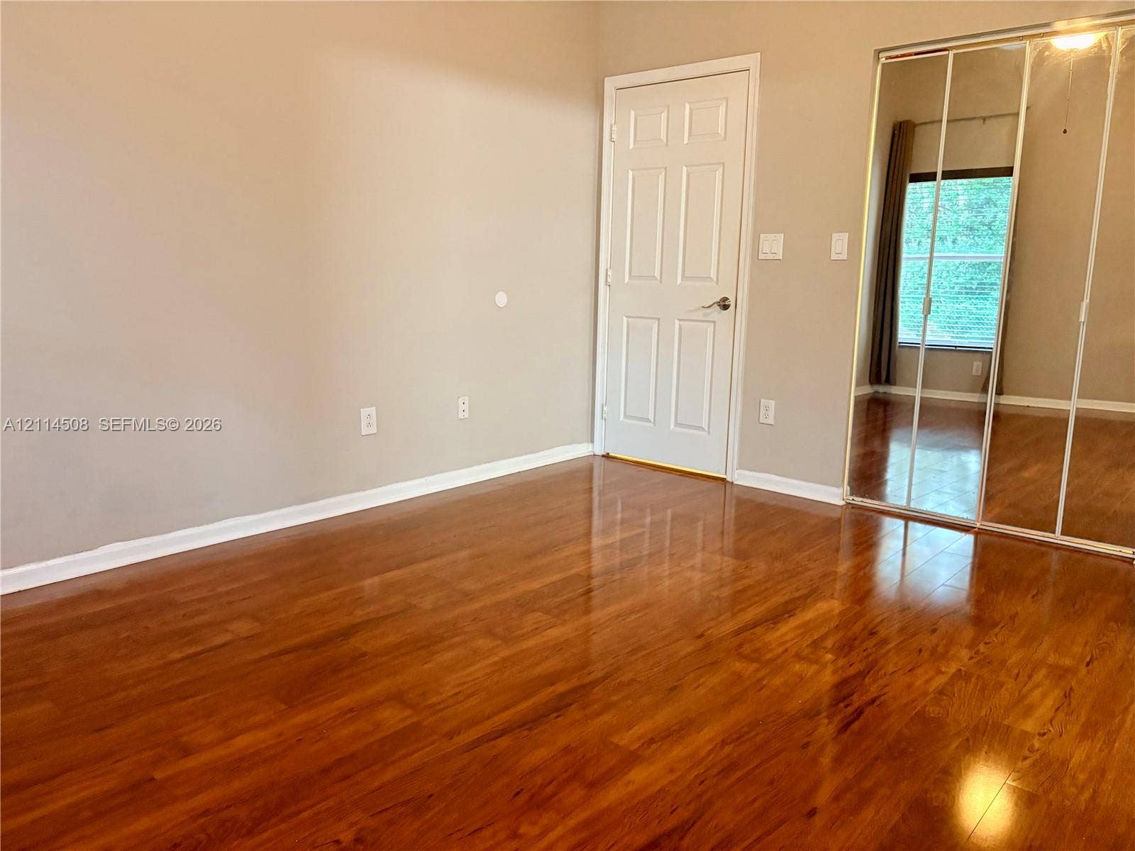 Room featuring wood-finish flooring, a neutral wall color palette, a classic six-panel interior door, and mirrored sliding closet doors