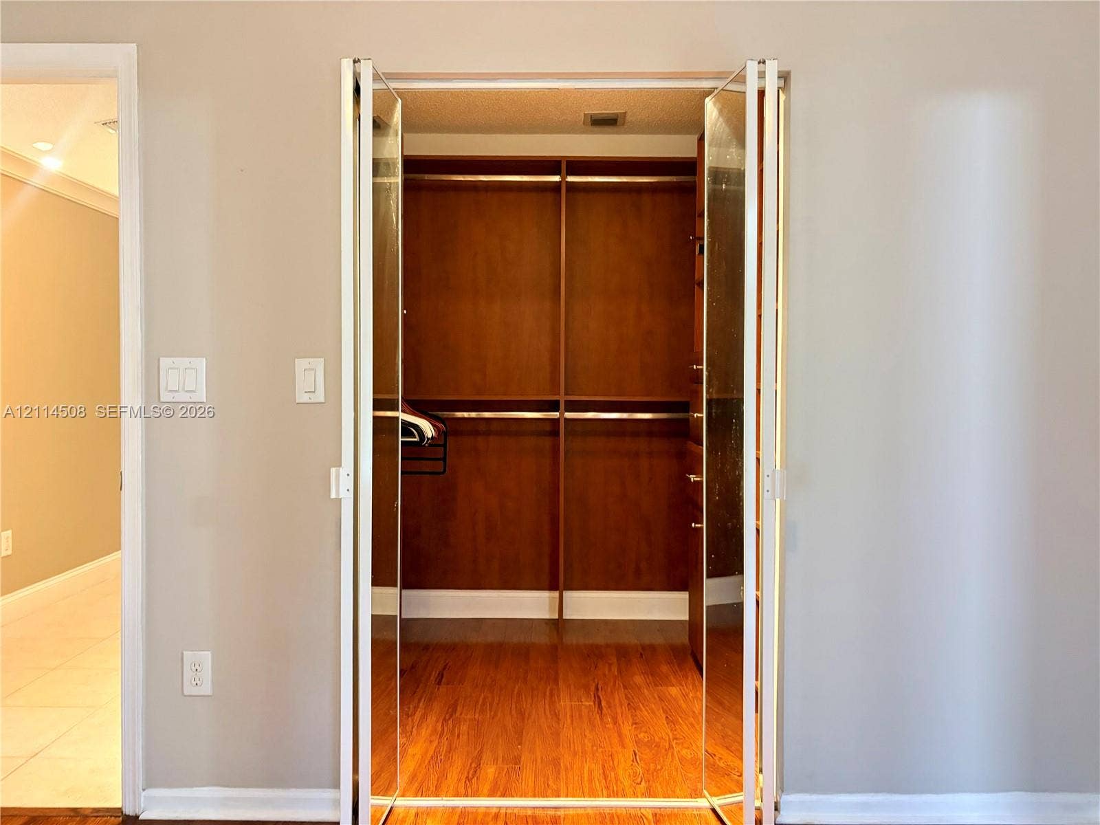 Walk-in closet featuring wood-finish flooring, built-in shelving, metal garment rods, and bifold glass-panel doors
