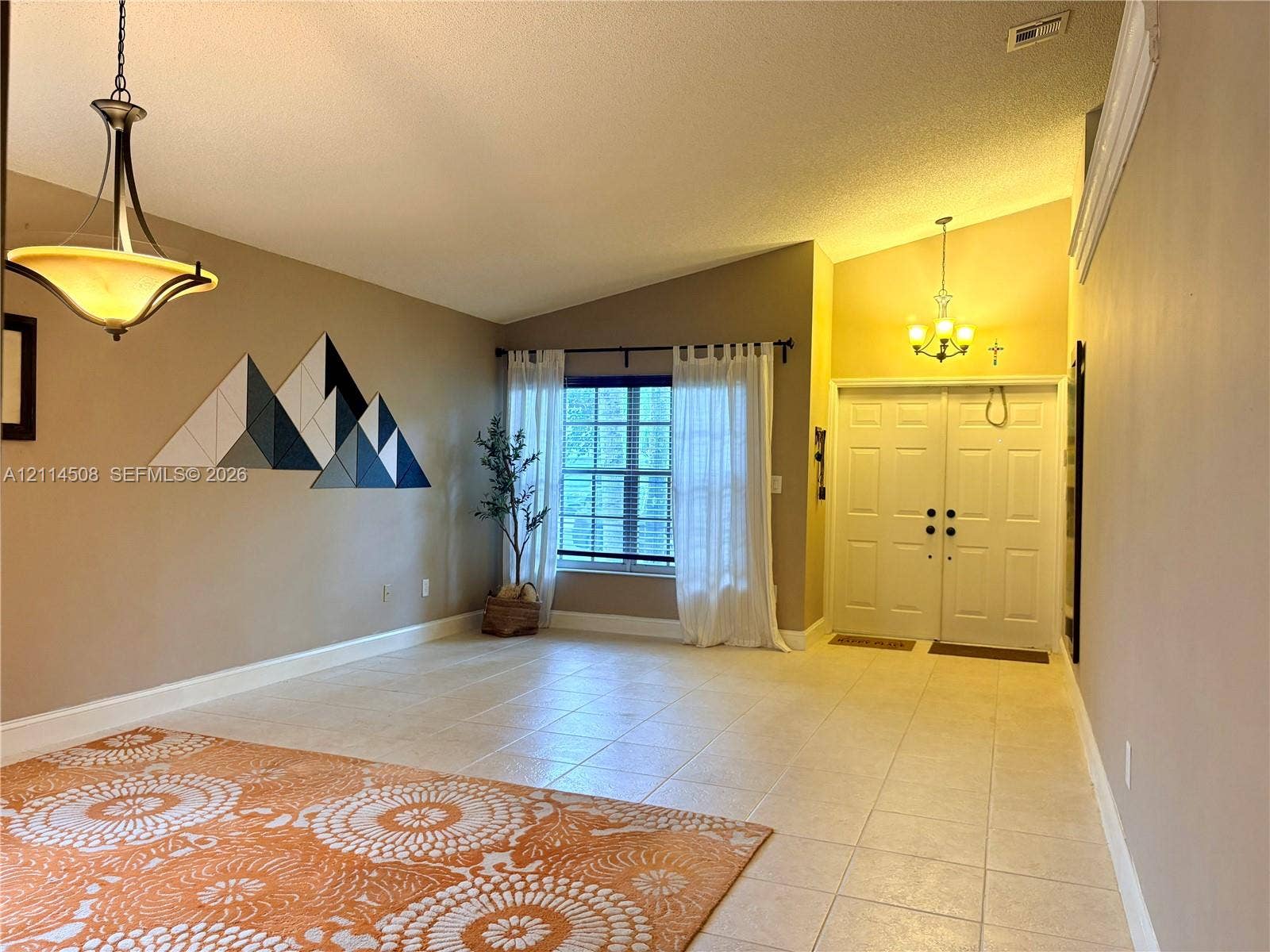 Vaulted ceilings featuring multi-tiered pendant lighting, tile flooring, and double-entry doors
