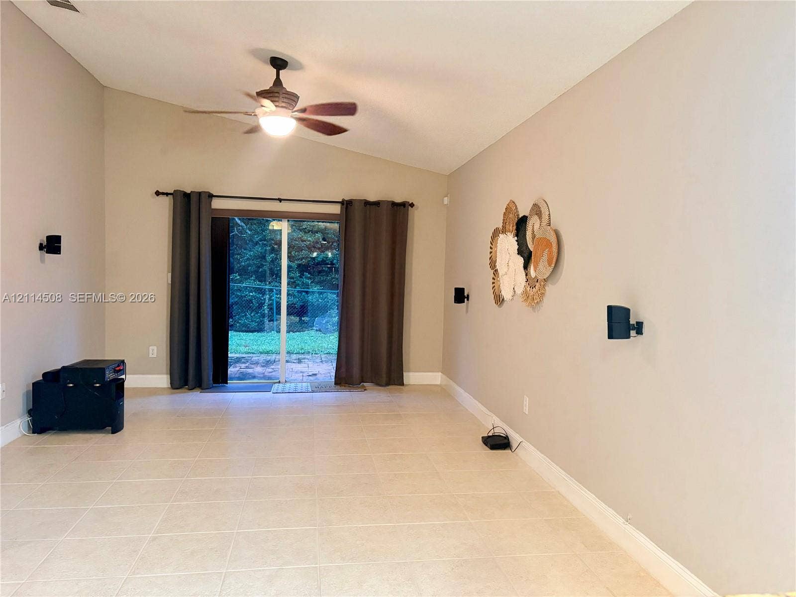 Vaulted ceiling, neutral tile flooring, ceiling fan with light fixture, and sliding glass door
