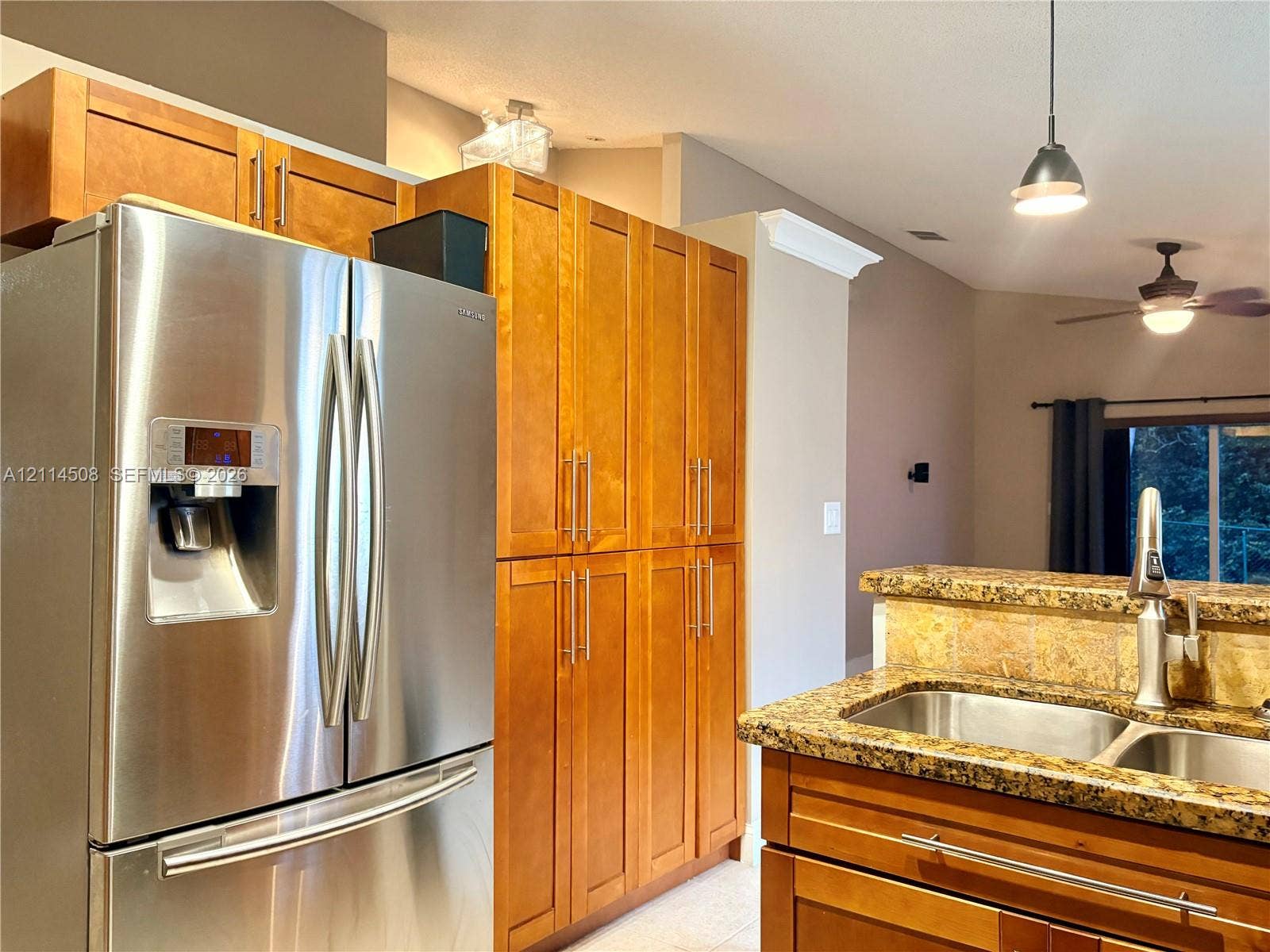 Kitchen featuring wood cabinetry, full-height pantry storage, stone-finish countertops, dual-basin stainless steel sink with high-arc faucet, and stainless steel French-door refrigerator