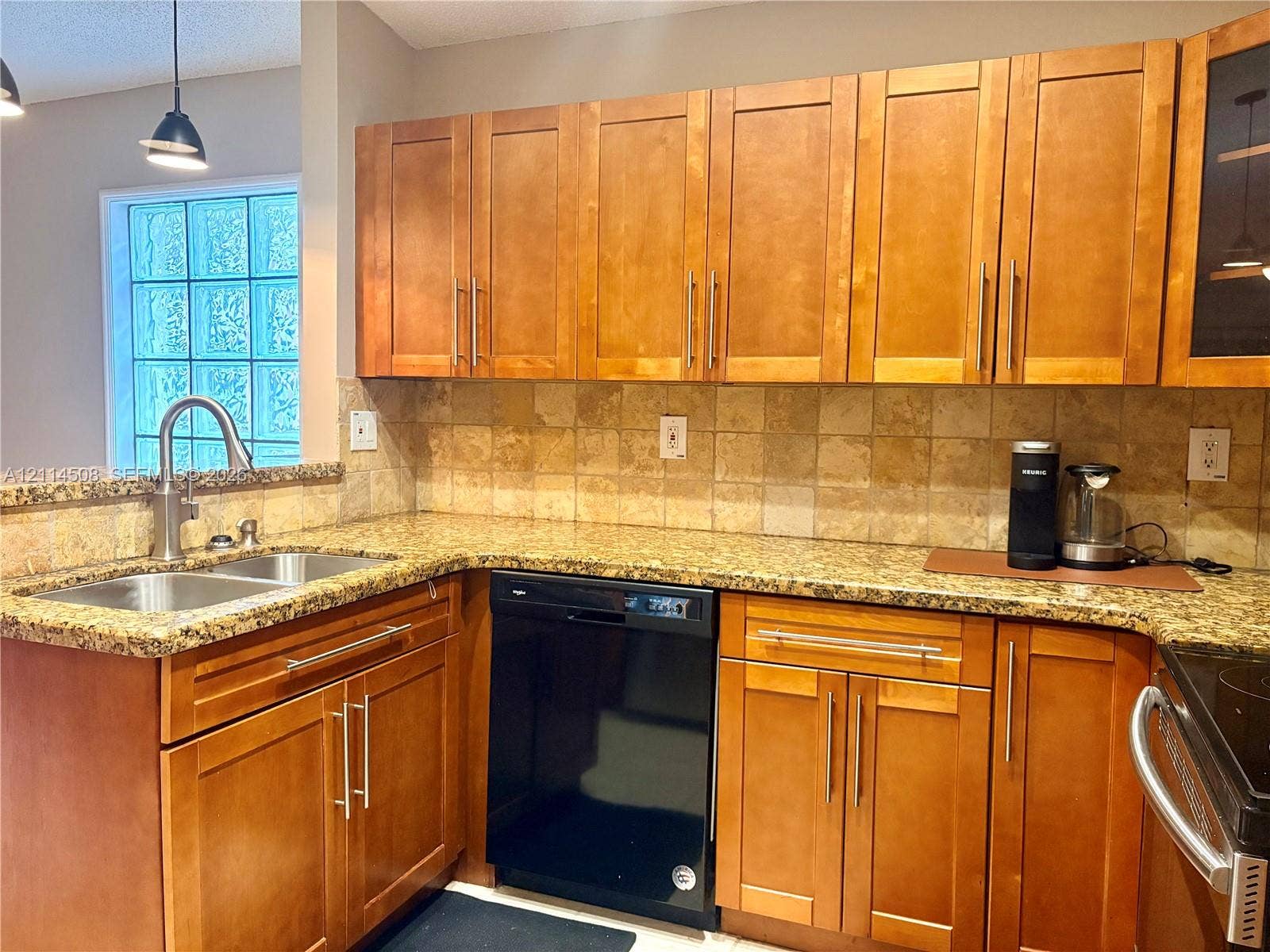 Kitchen featuring shaker-style wood cabinetry, stone countertops, square-tile backsplash, stainless steel dual-basin undermount sink with gooseneck faucet, and glass block window