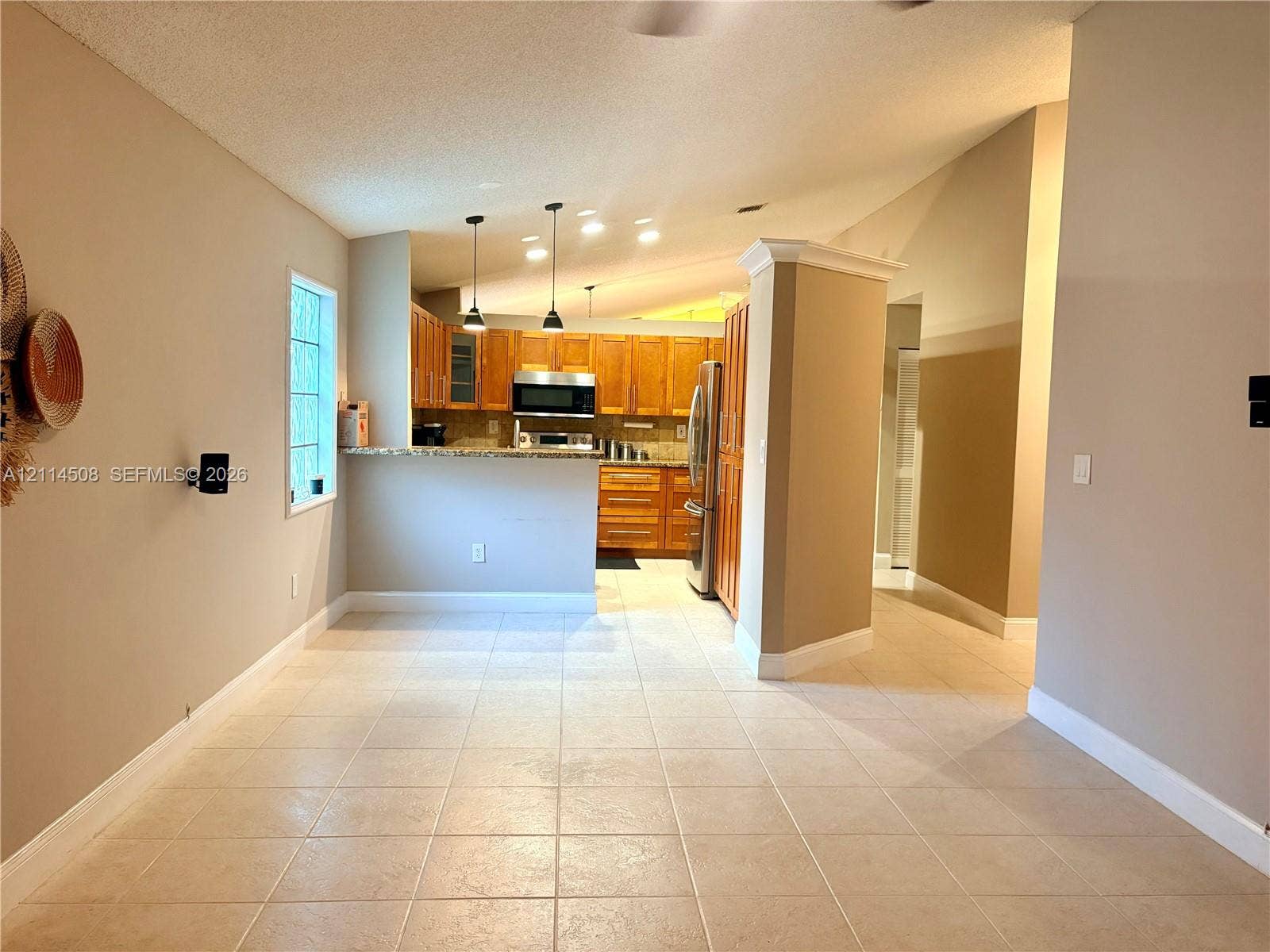 Kitchen featuring wood cabinetry, stone countertops, stainless steel appliances, pendant lighting, and tile flooring