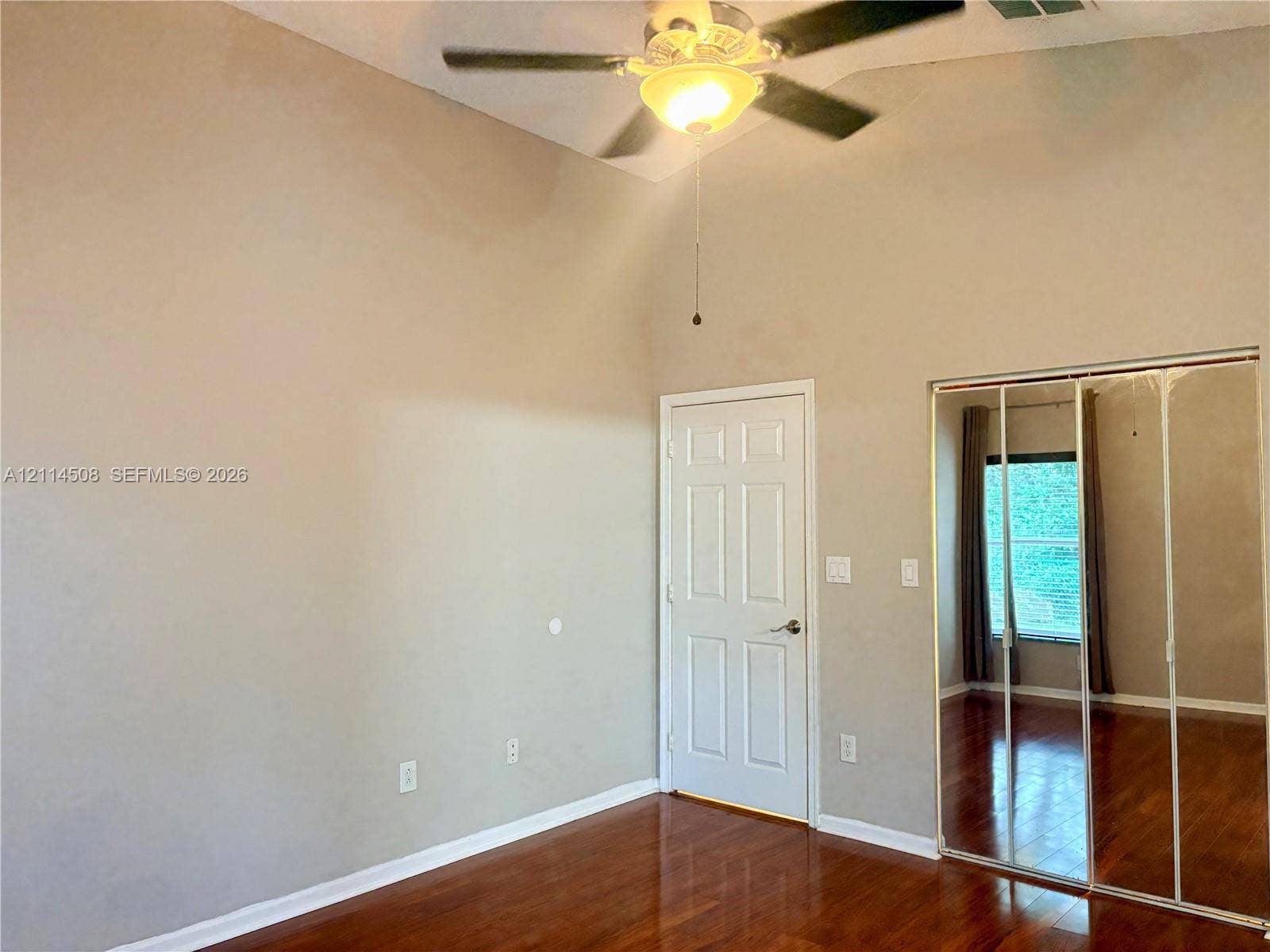 Vaulted ceiling with a centrally mounted lighted ceiling fan, wood-finish flooring, and closet featuring mirrored sliding doors