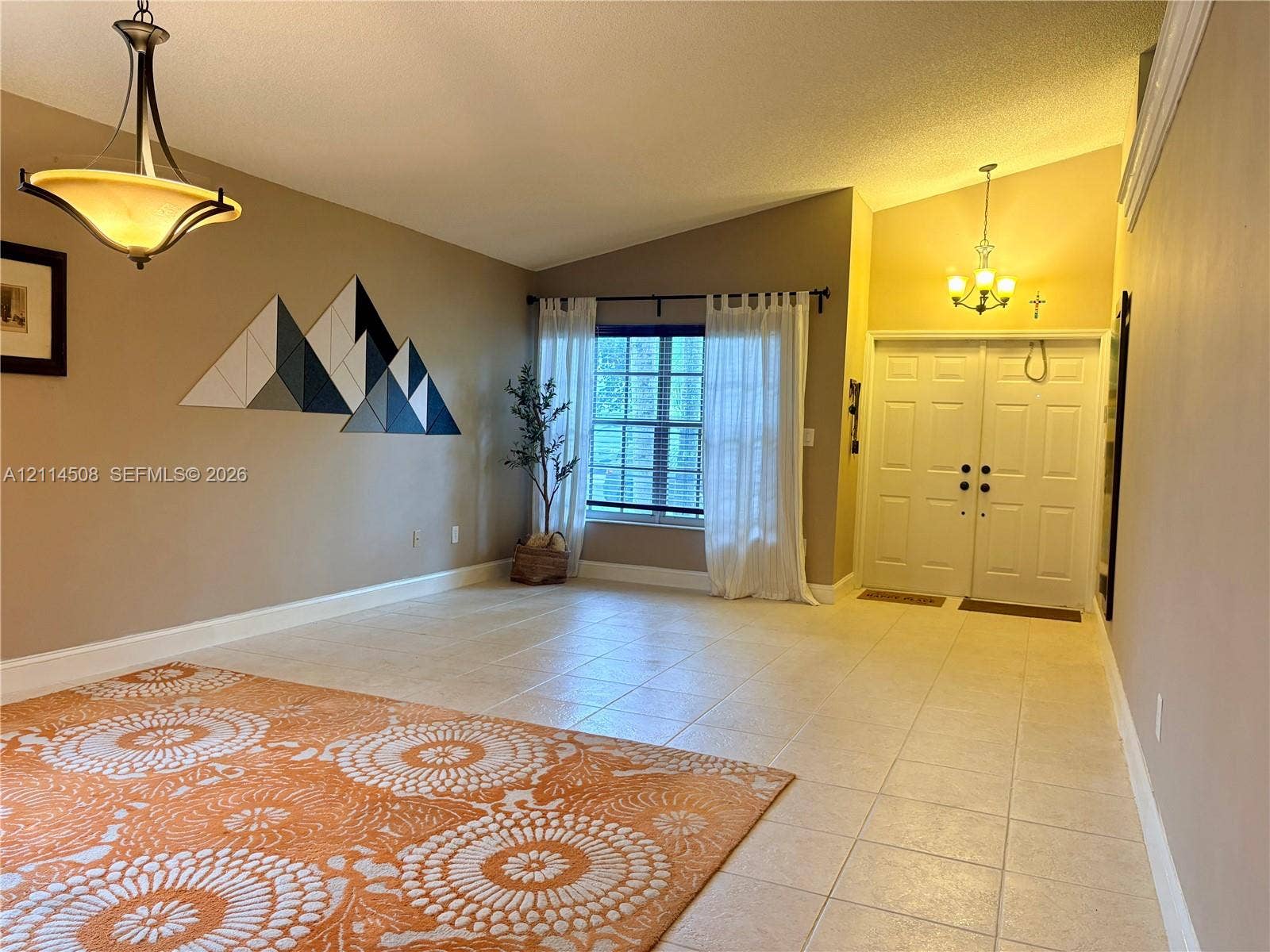 Vaulted ceilings, large-format tile flooring, double-entry front doors, and dual decorative chandeliers