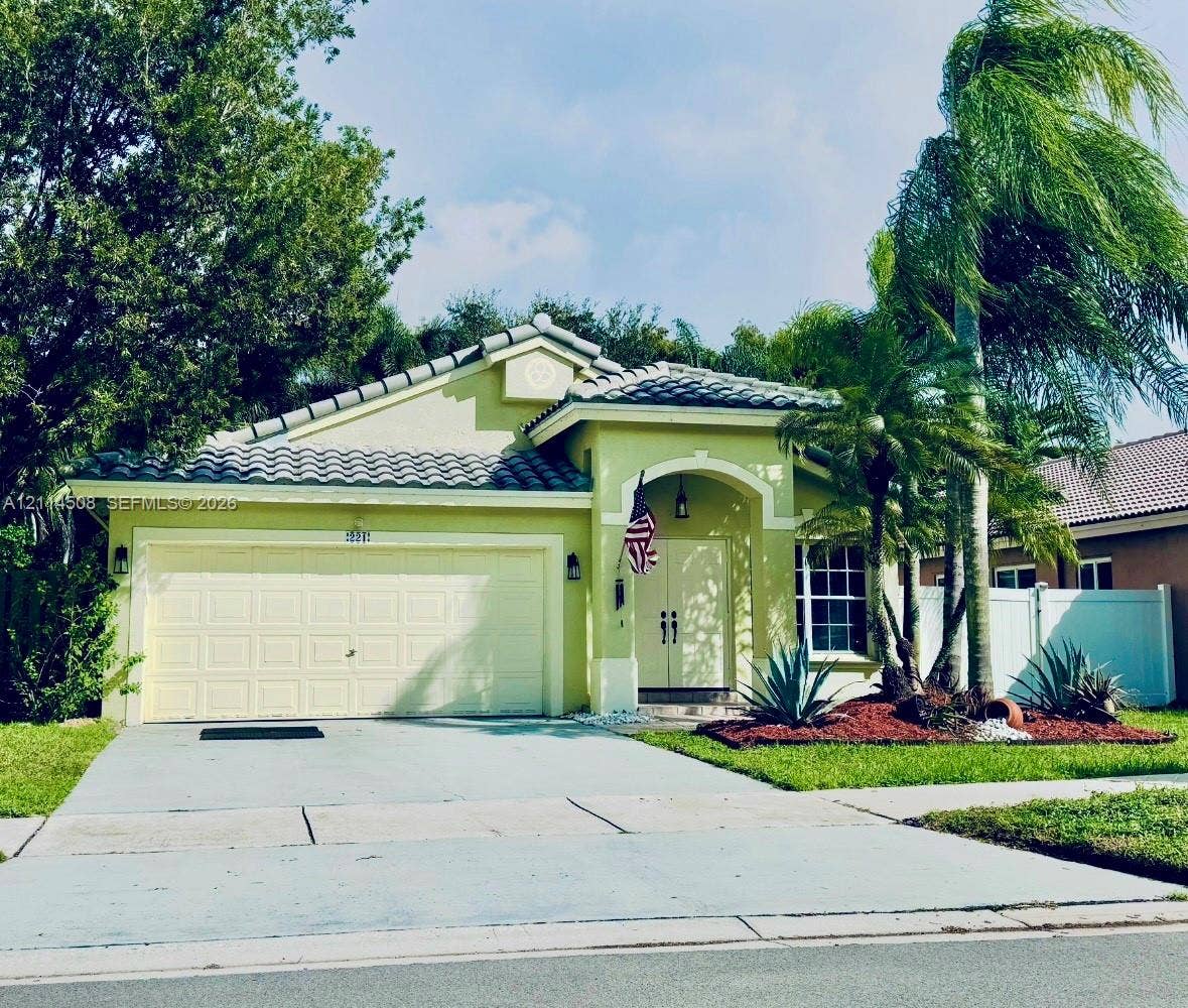 Stucco exterior featuring a tiled roof, arched entryway, double-door entrance, two-car garage, and established landscaping